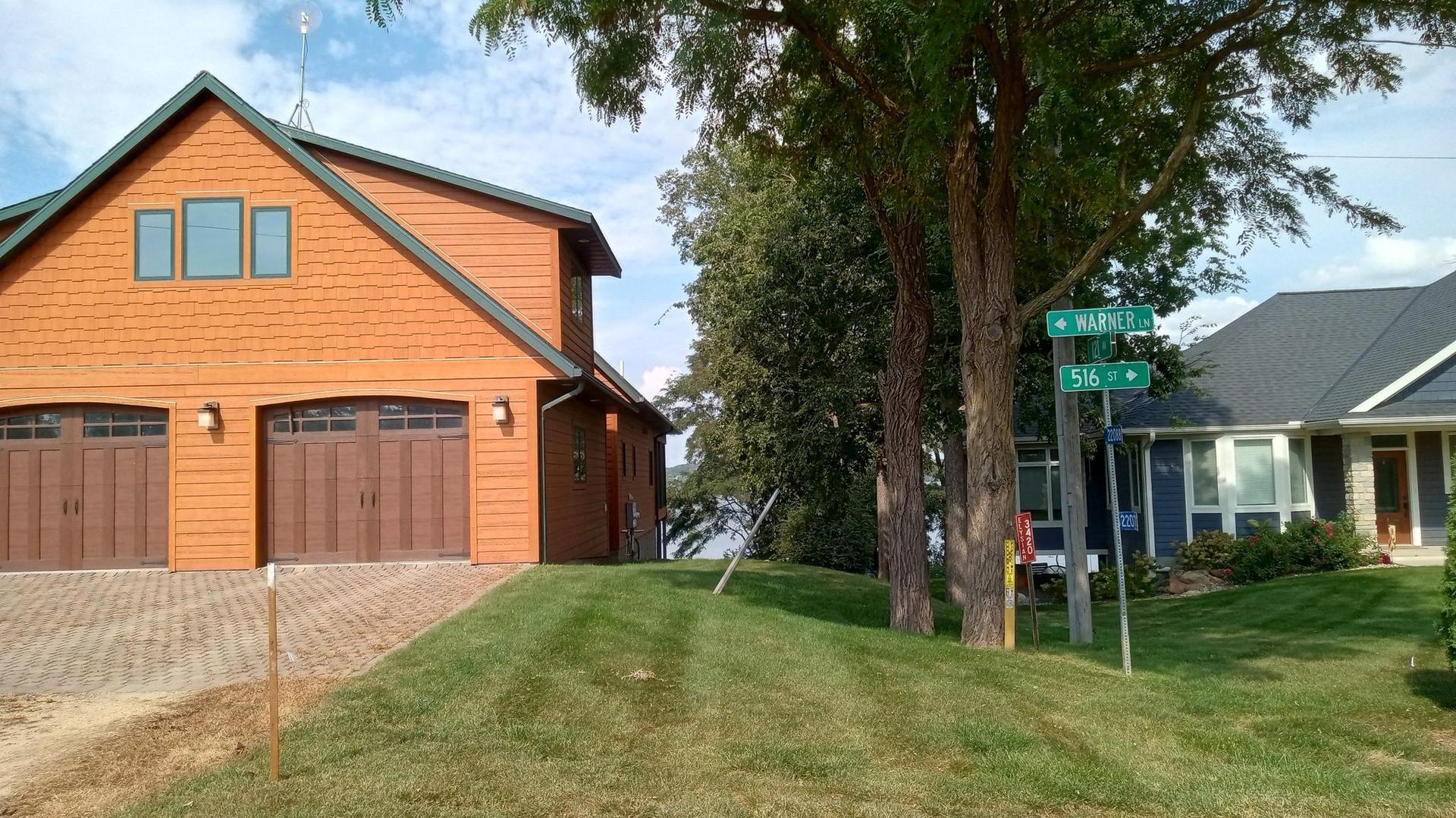 Two houses and a street sign on a grassy hill on a sunny day.