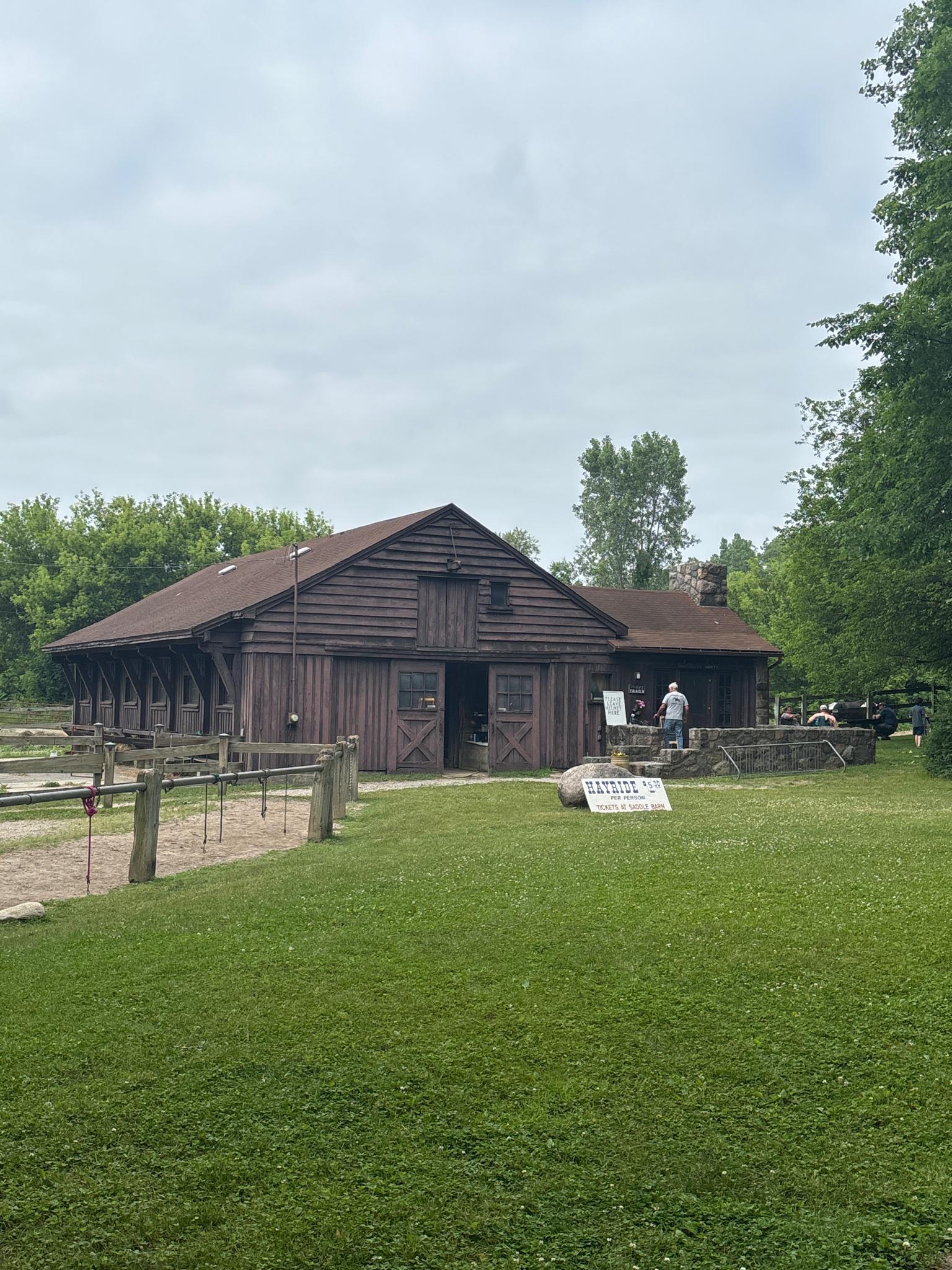 A large dark wooden barn with a person standing outside on a cloudy day.