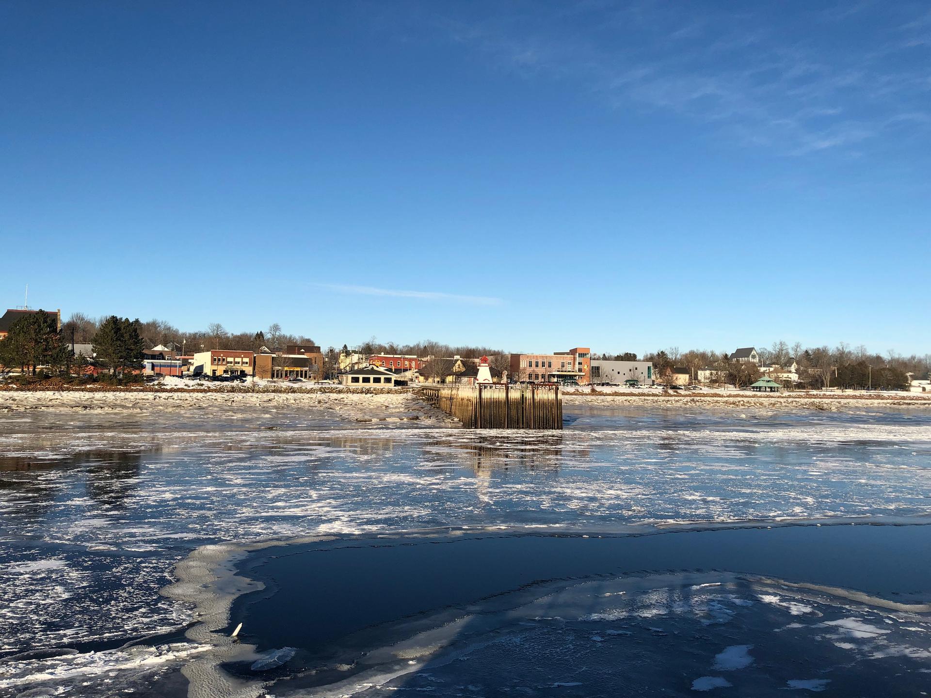 Icy river with a distant town under a clear blue winter sky.