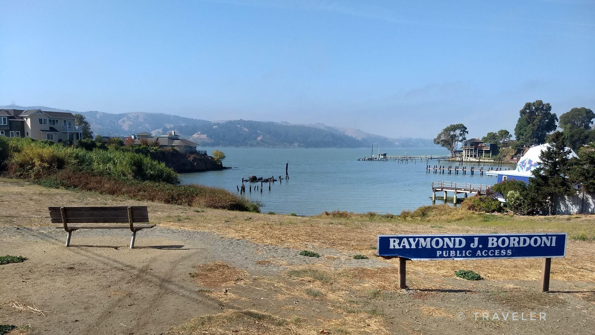 Sunny bay view from a park bench, with a public access sign.