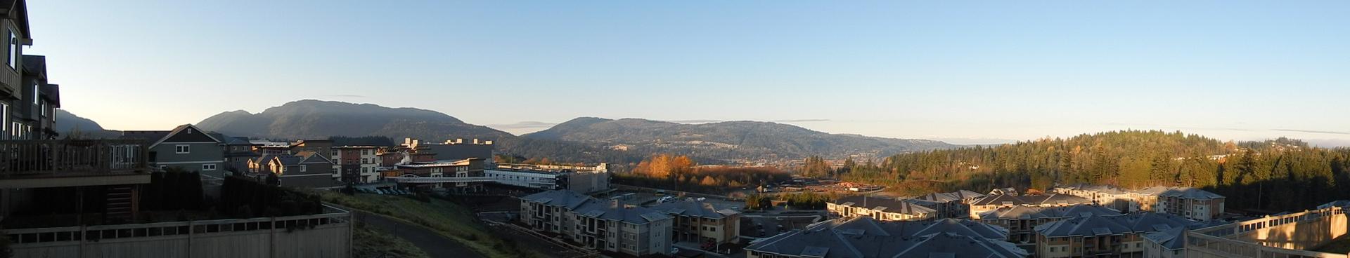 Panoramic view of buildings, distant mountains, and trees under a clear sky.