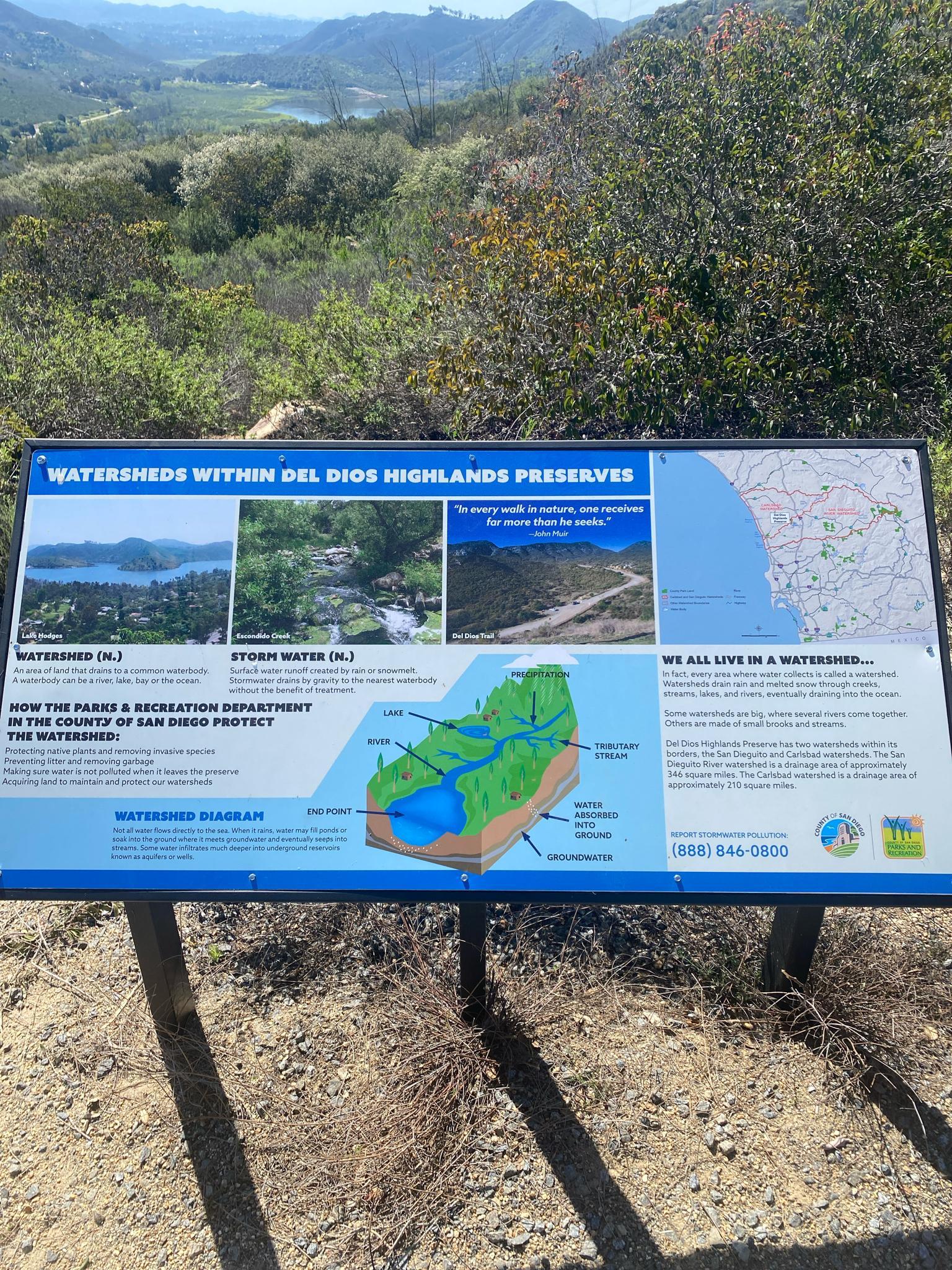 Informational sign about watersheds with green hills in the background.