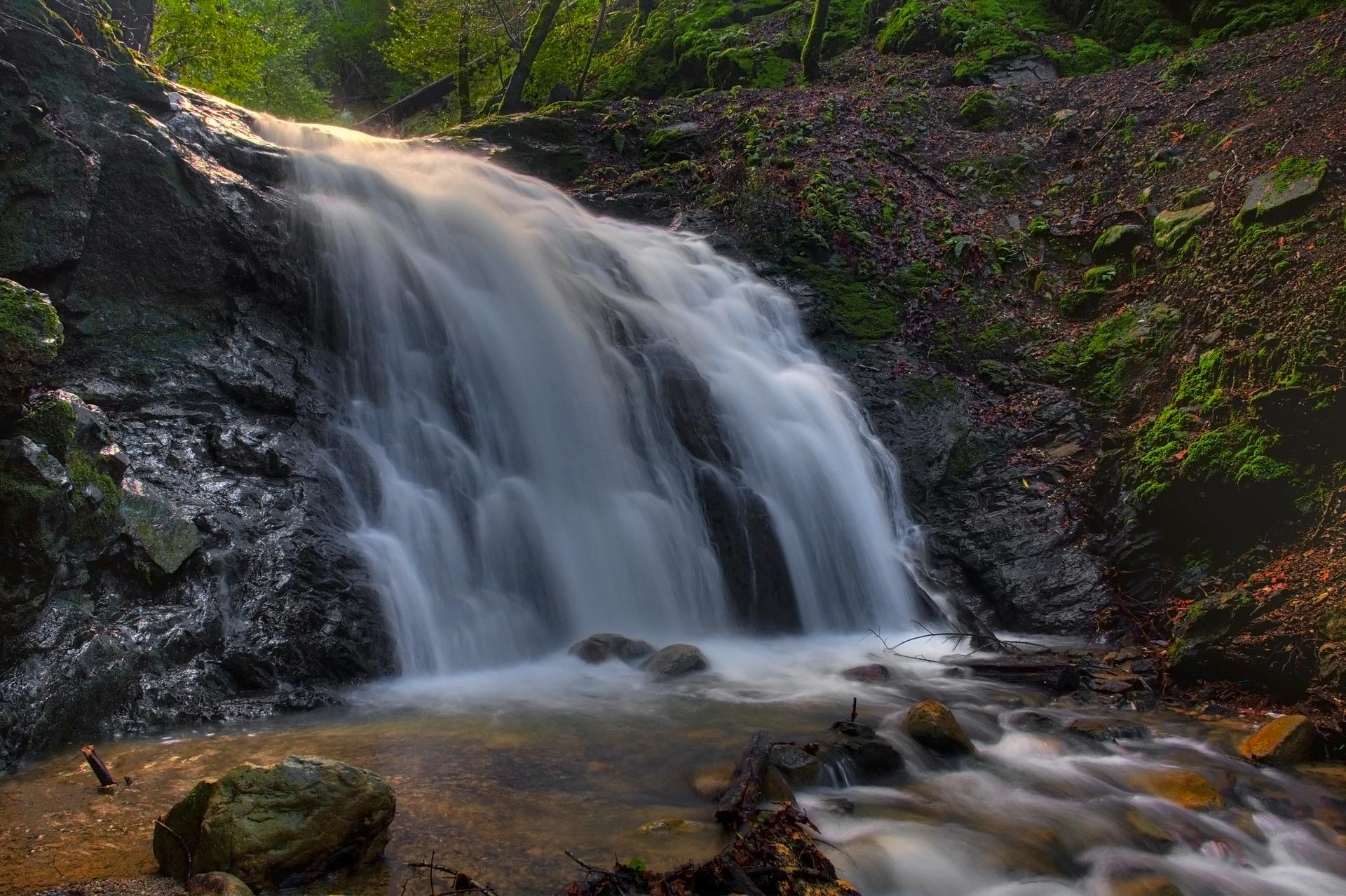 A wide, flowing waterfall with blurred water, surrounded by lush forest.