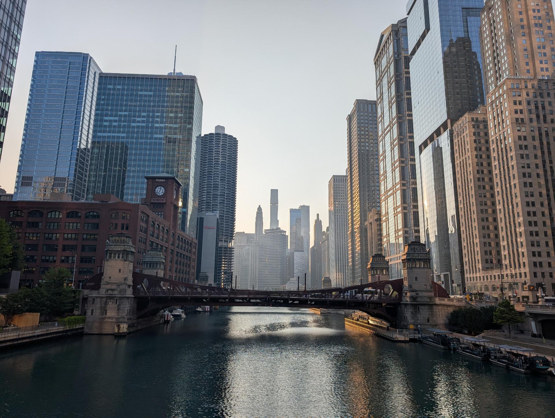A river flows through a city with tall buildings and a bridge in hazy light.