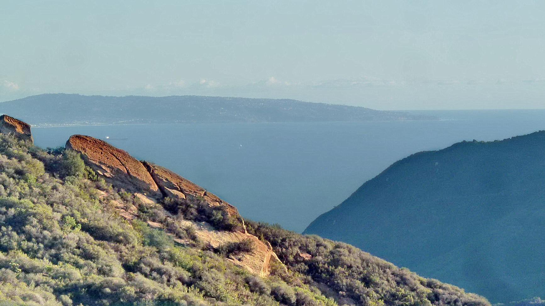 Distant ocean view beyond a rocky, brush-covered mountain range.