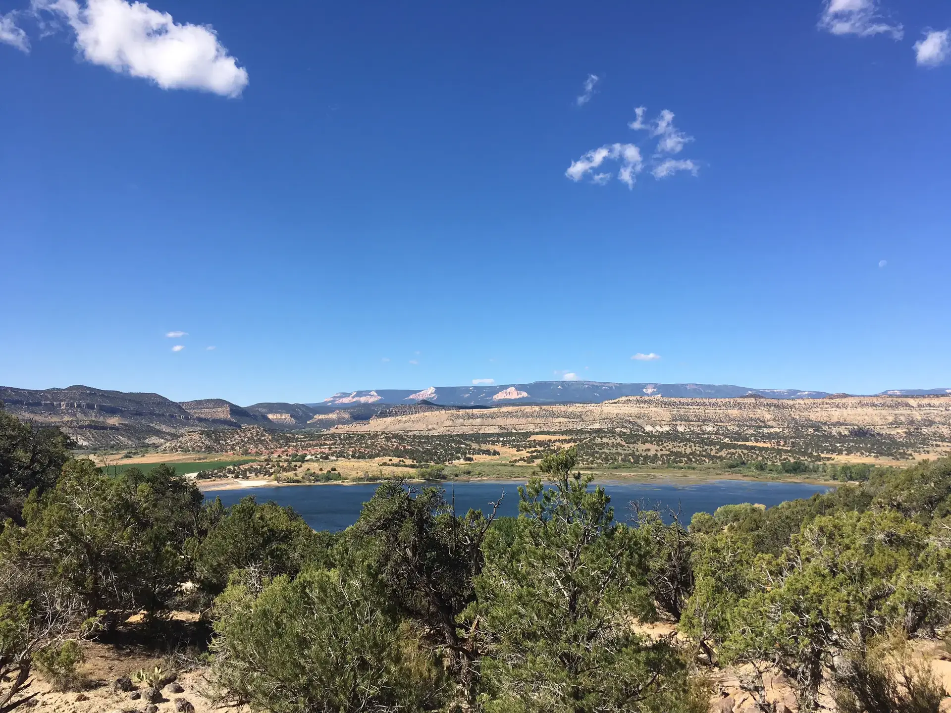 Panoramic view of a large lake surrounded by arid mountains under a bright blue sky.