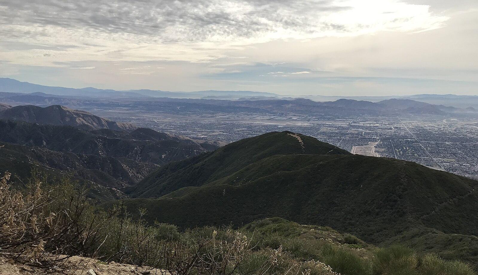 Expansive view of green mountains and a distant city under an overcast sky.