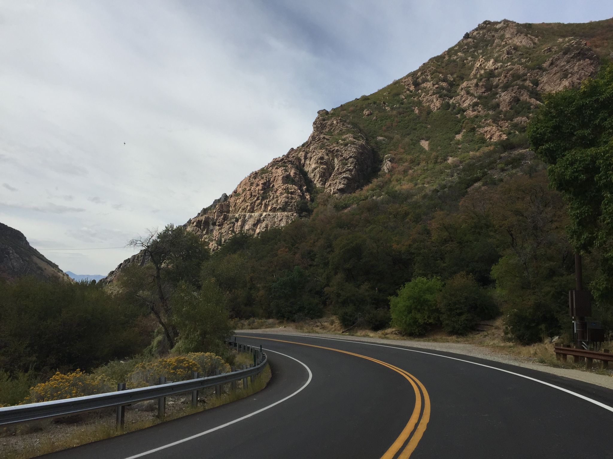 Winding road curves past a rocky, vegetated mountain under a cloudy sky. - Granite Flume Trail