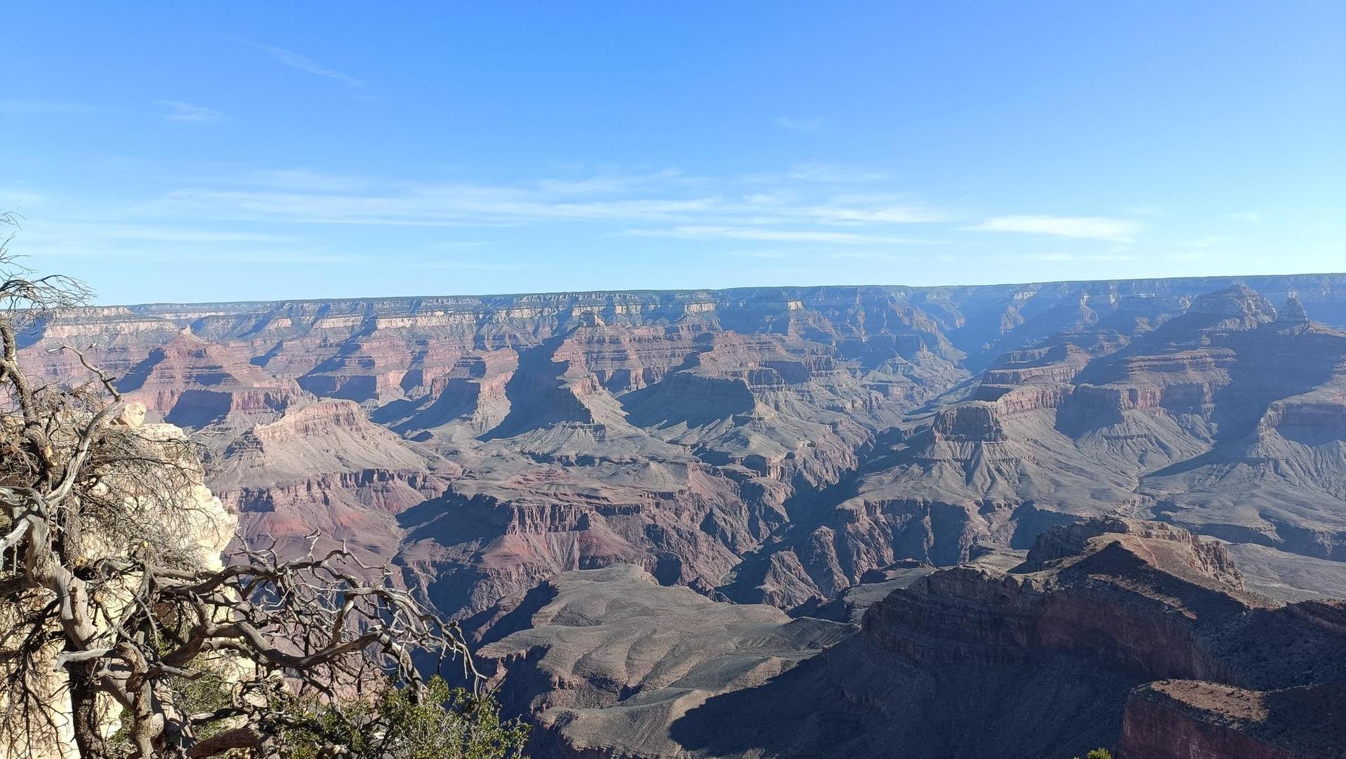 Wide canyon landscape under clear blue sky, showing distant rock formations.
