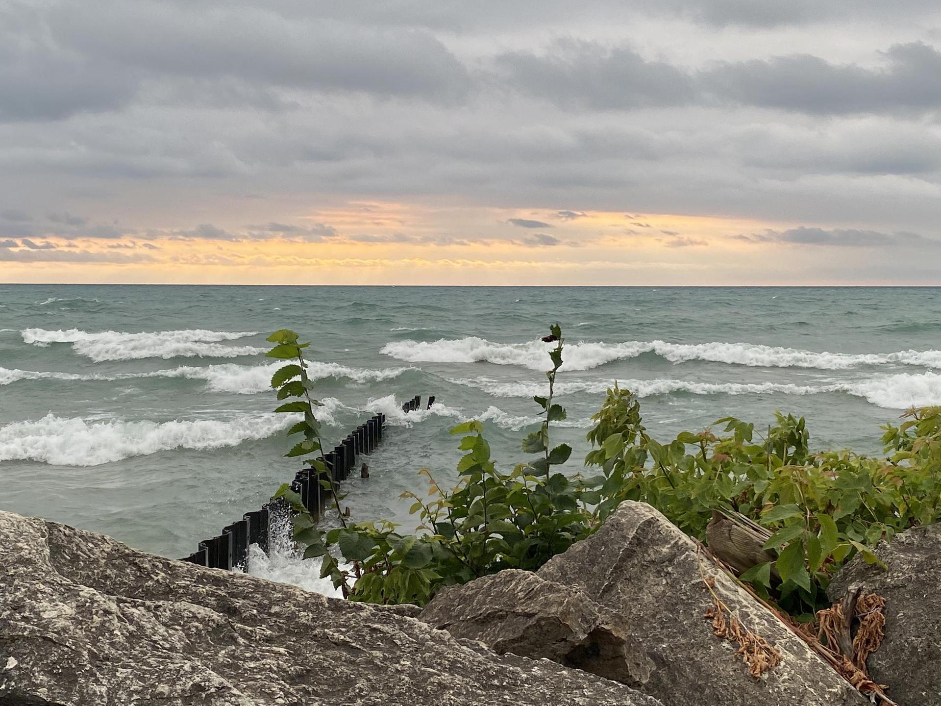 Rough waves crashing against a wooden pier, viewed from rocky shore.