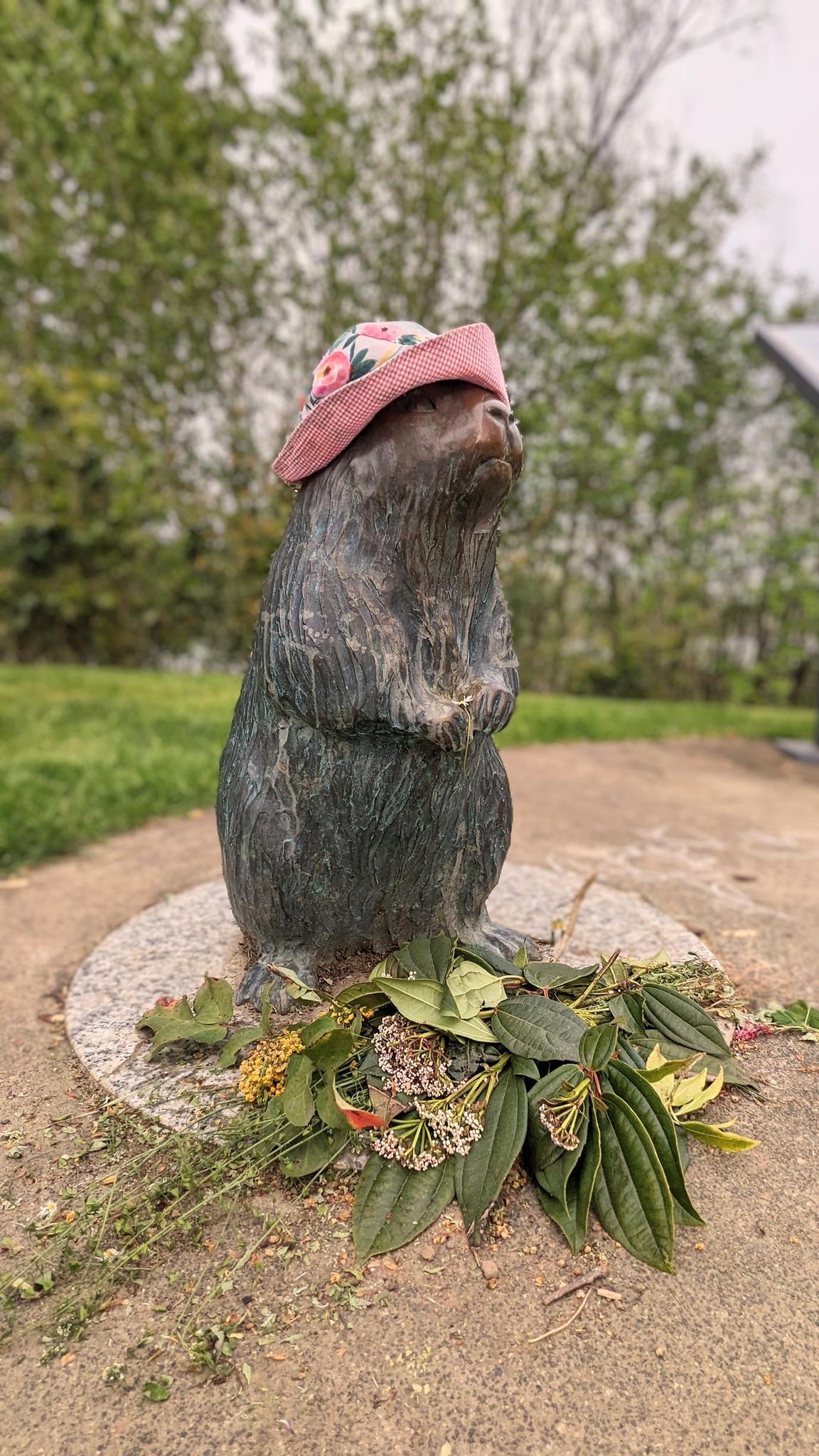 A charming animal statue wearing a pink floral hat, adorned with flowers.