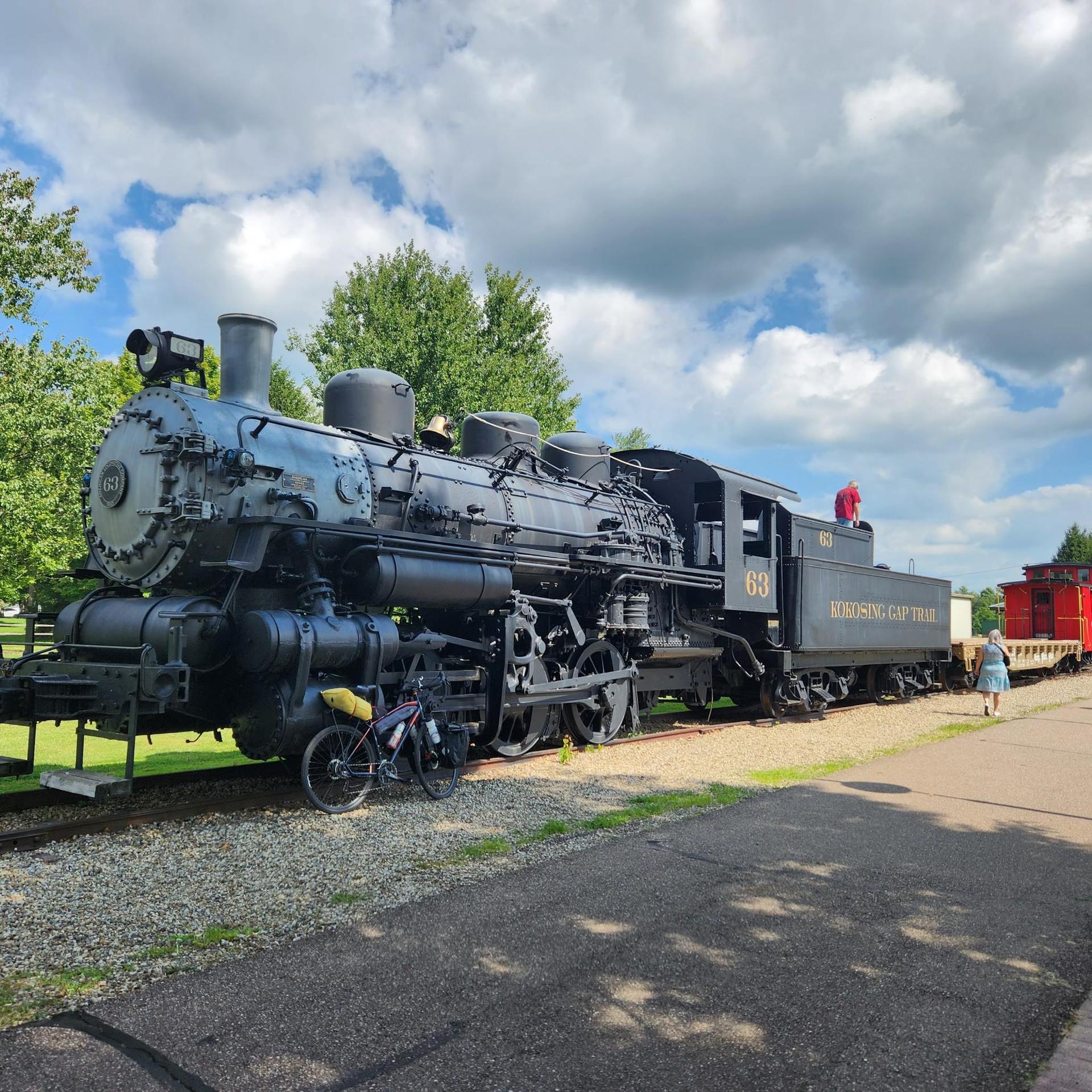 Historic black steam locomotive on tracks with a person nearby under cloudy sky.