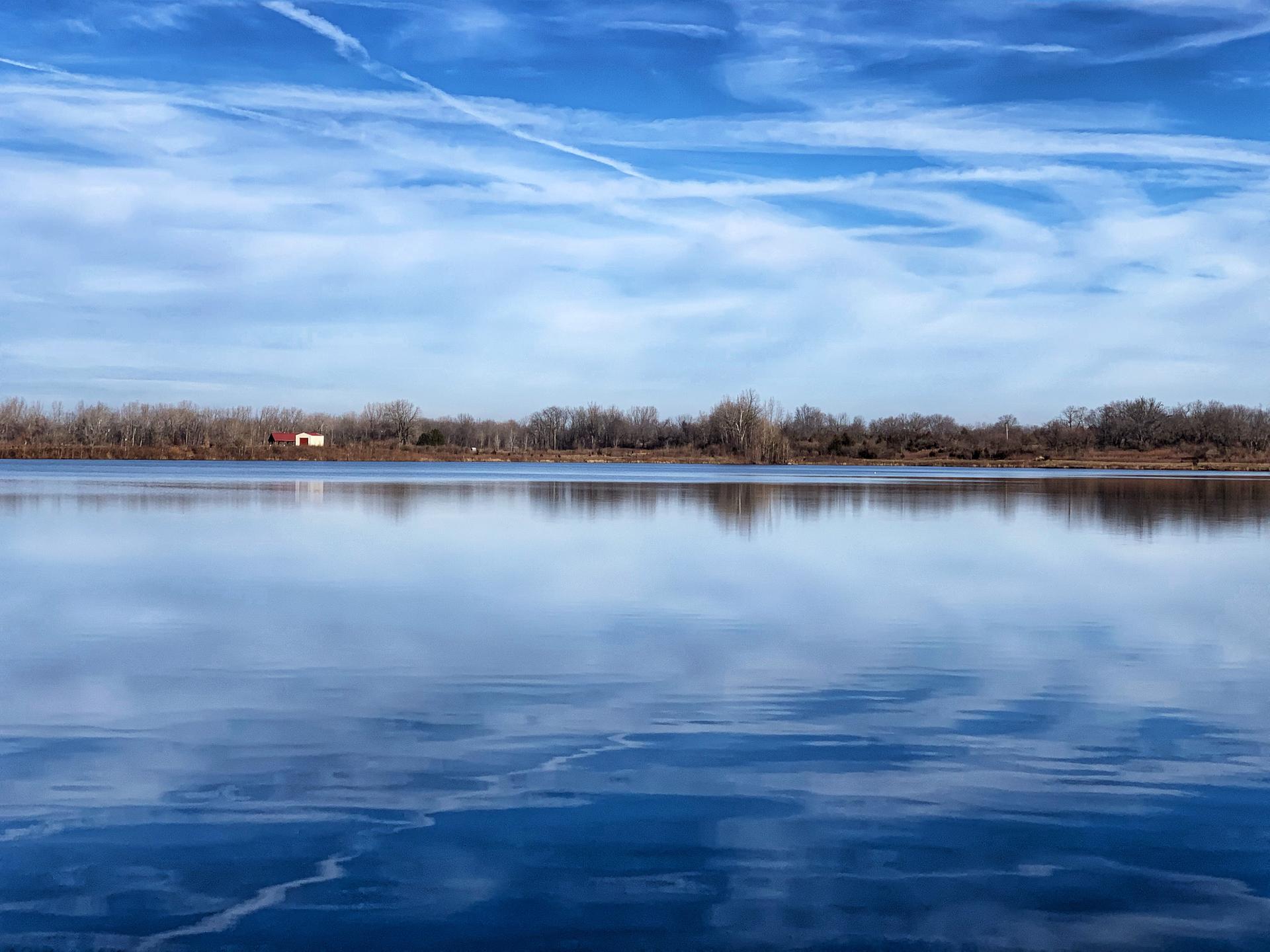 Calm lake reflecting a bright blue sky with a distant treeline.