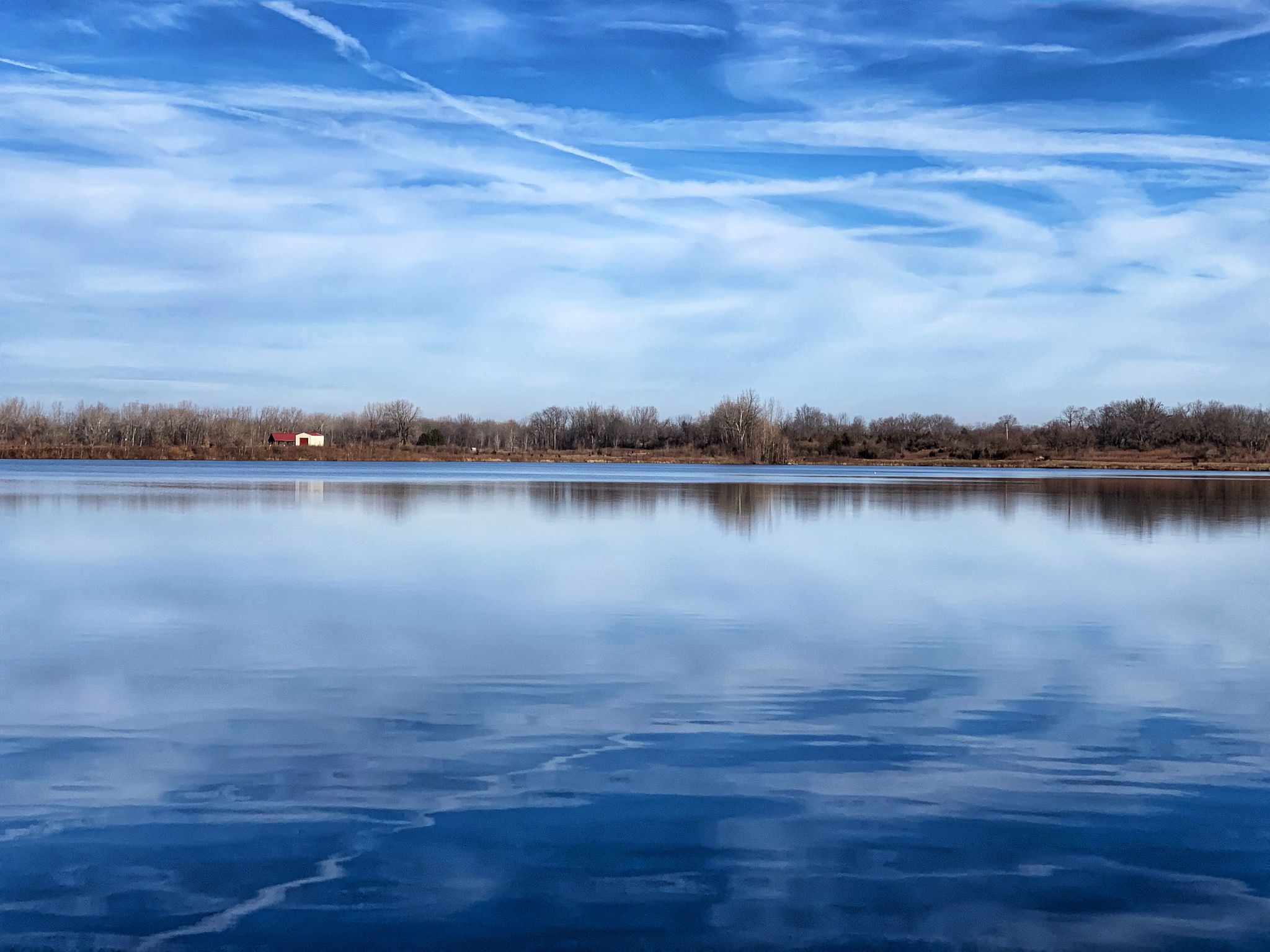 Calm lake reflecting a bright blue sky with a distant treeline. - Hilliard to Harrisburg loop via Prairie Oaks Metro Park