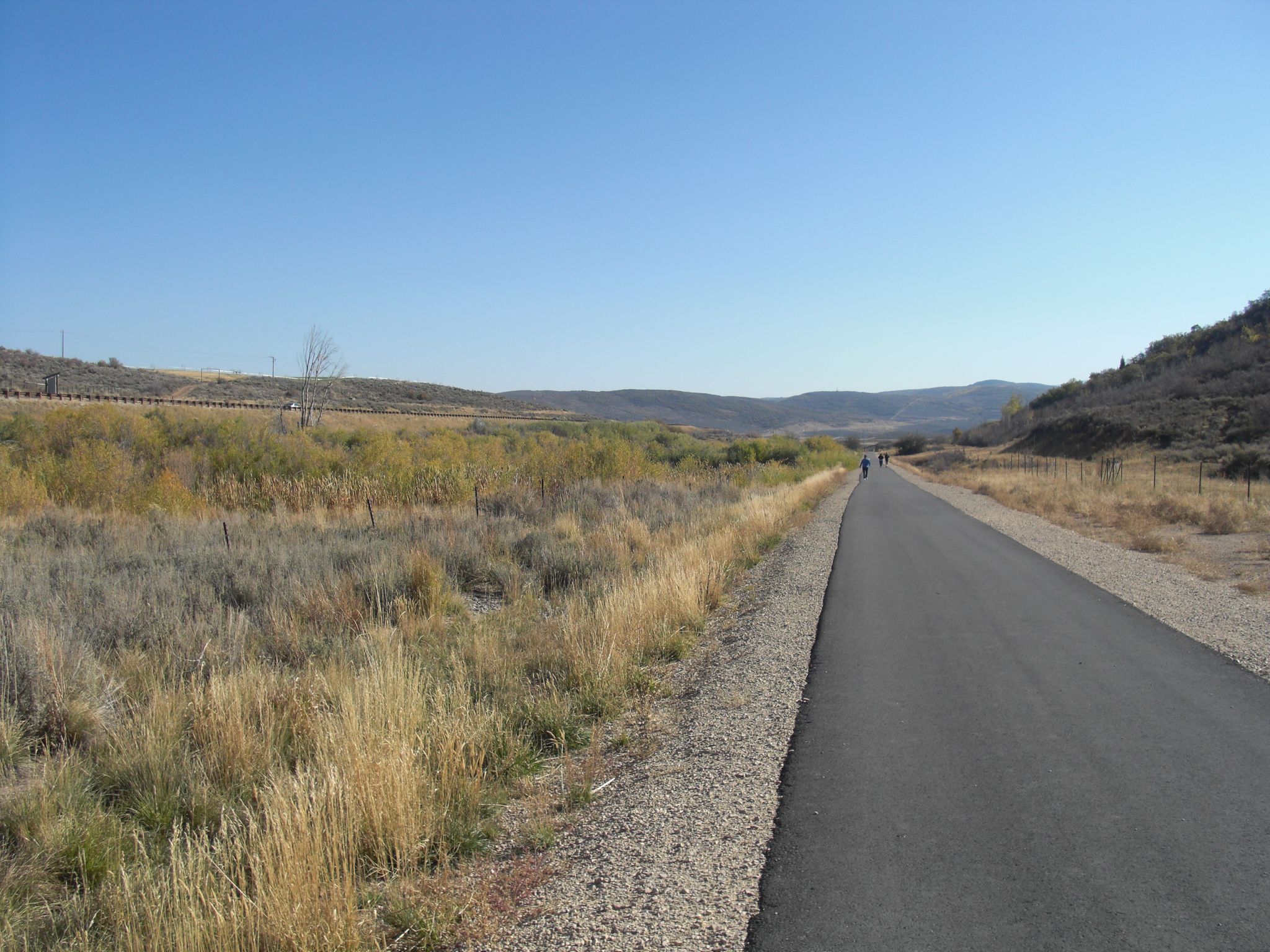 Paved path through dry grass and hills, with people walking in the distance. - Park City to Kamas via Union Pacific Rail Trail