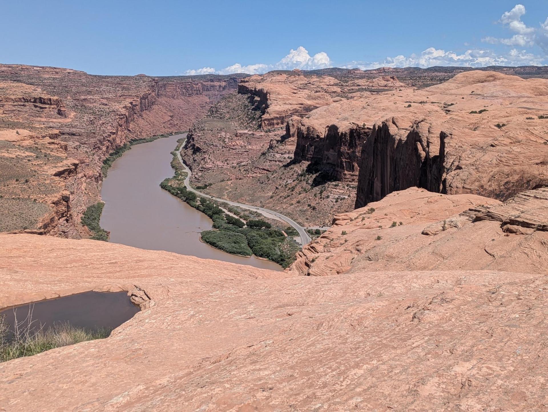 A wide river winds through a vast red rock canyon on a sunny day.
