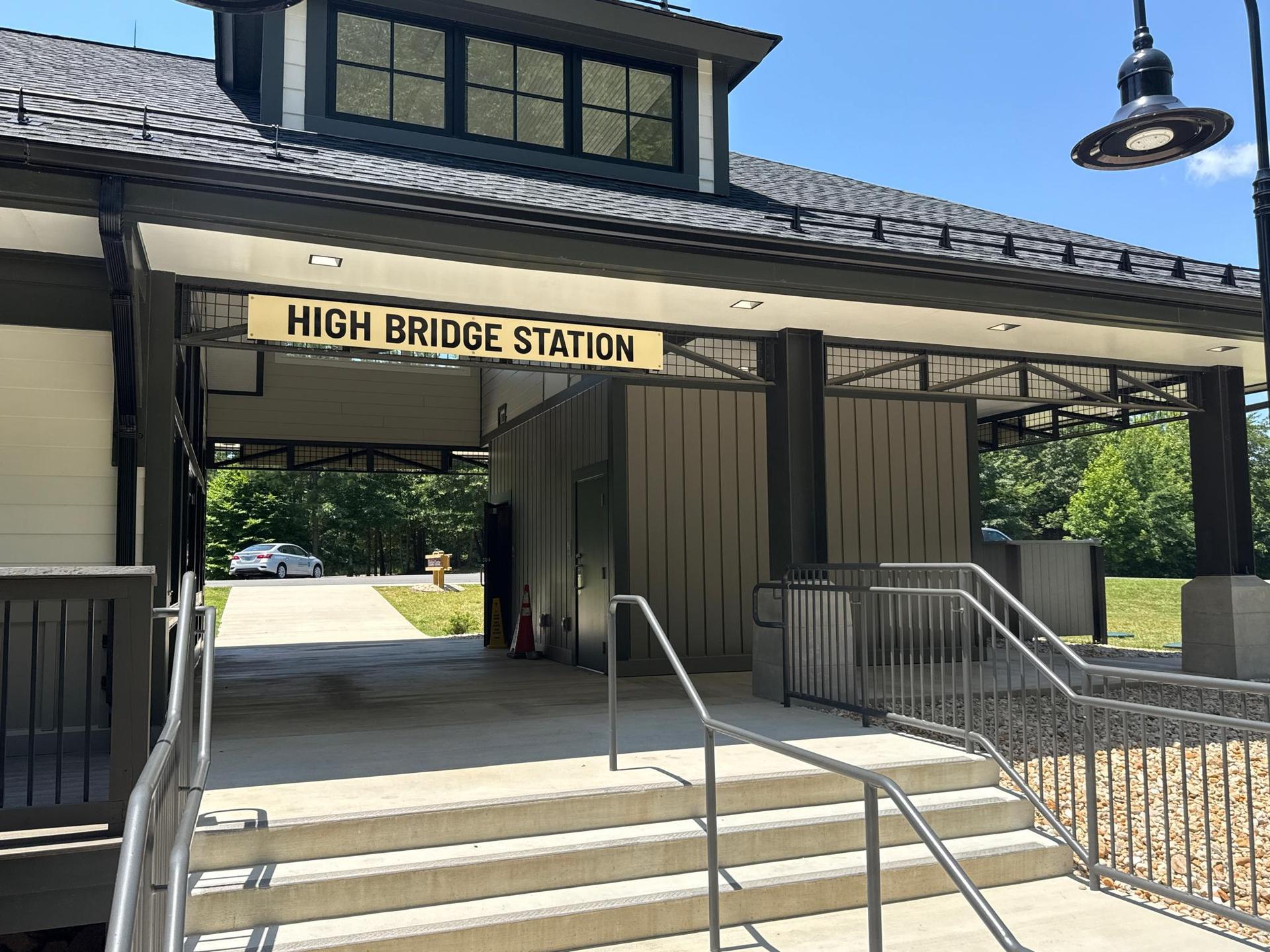 A modern building entrance with a 'HIGH BRIDGE STATION' sign, sunny.