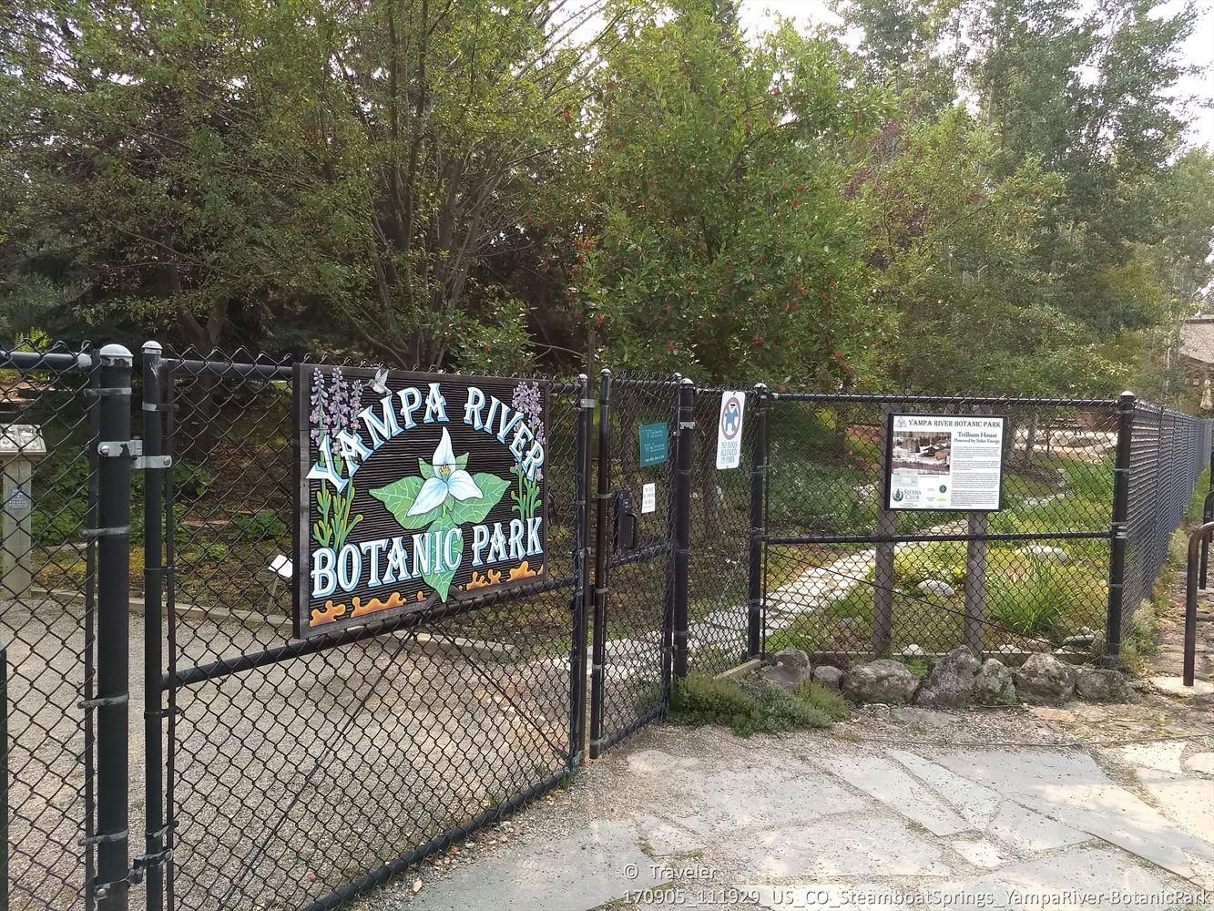 A black chain-link fence gate with a sign, leading to a lush green park. - Yampa River Core Trail