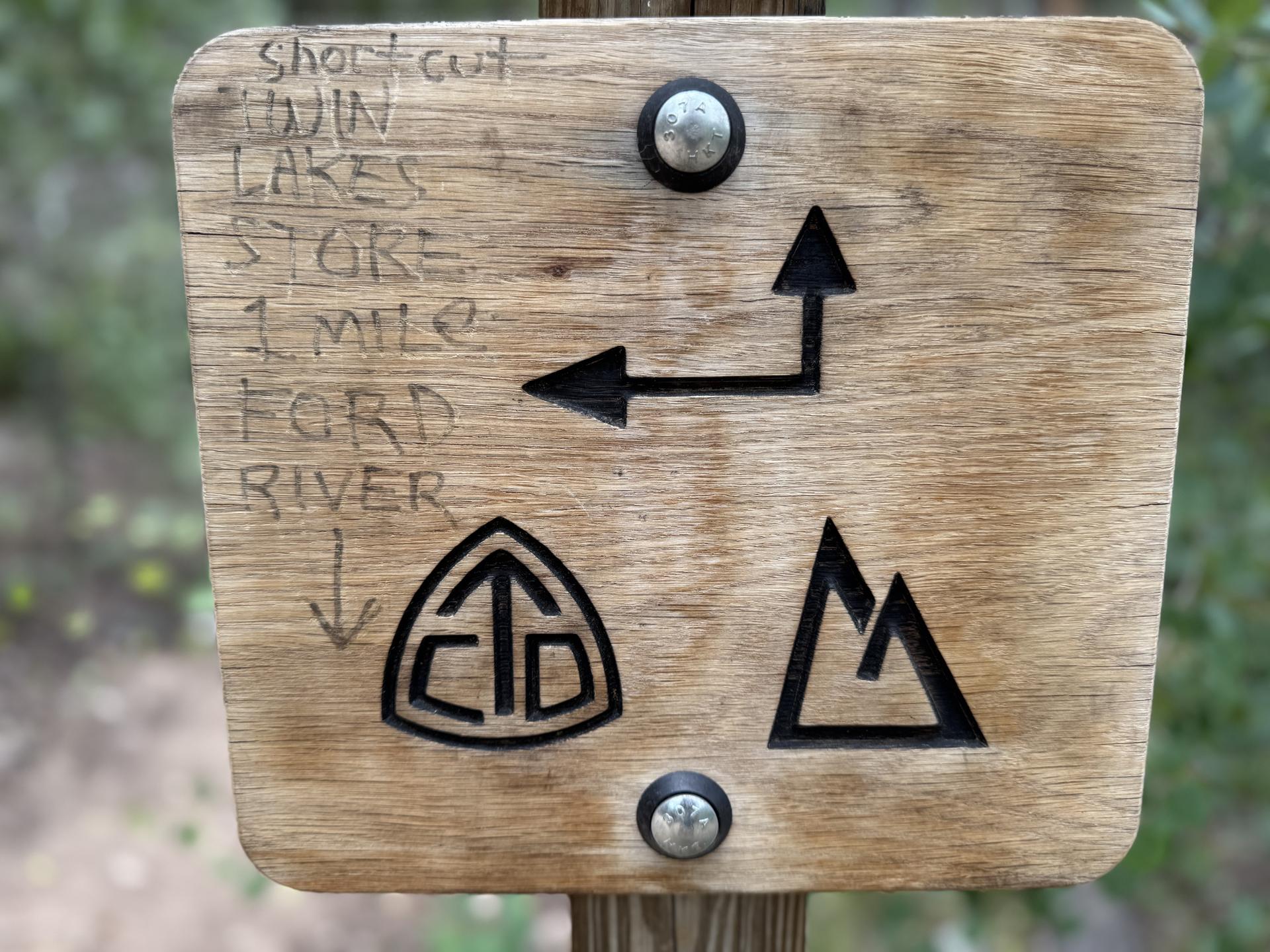 Close-up of a wooden trail sign with arrows and symbols.