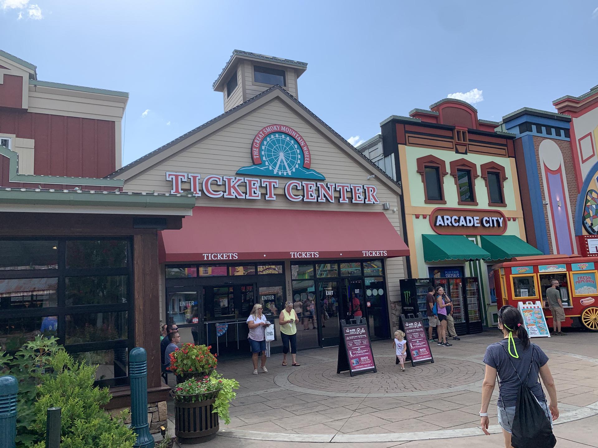 Ticket center building with people outside, next to an arcade, under bright sun.