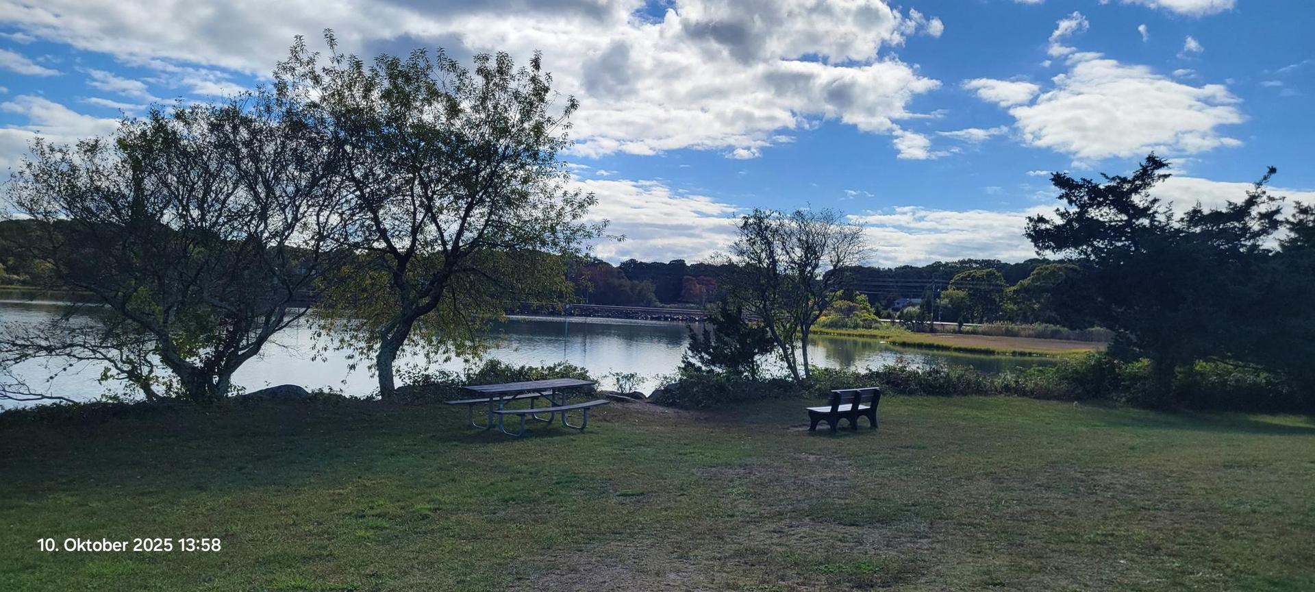 Picnic area by a calm lake, surrounded by trees under a cloudy sky.