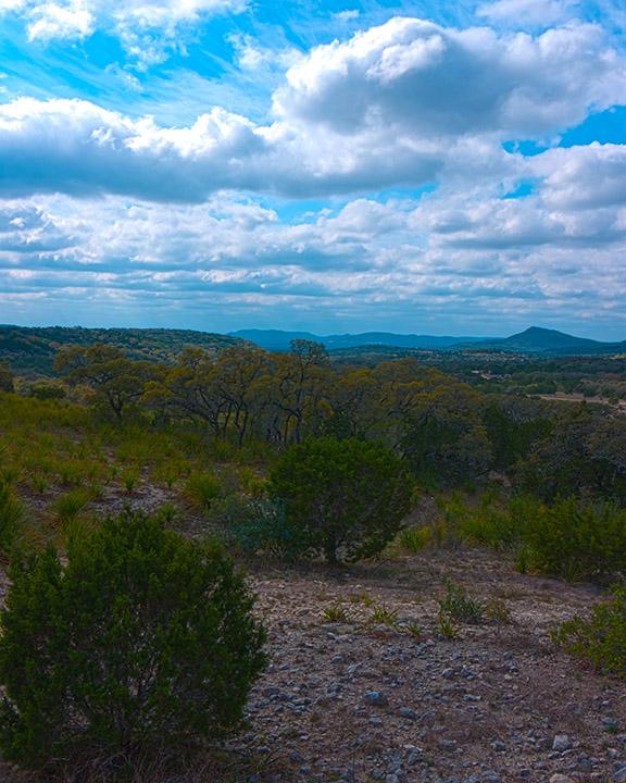 Expansive landscape with green trees, rolling hills, and a bright cloudy sky.