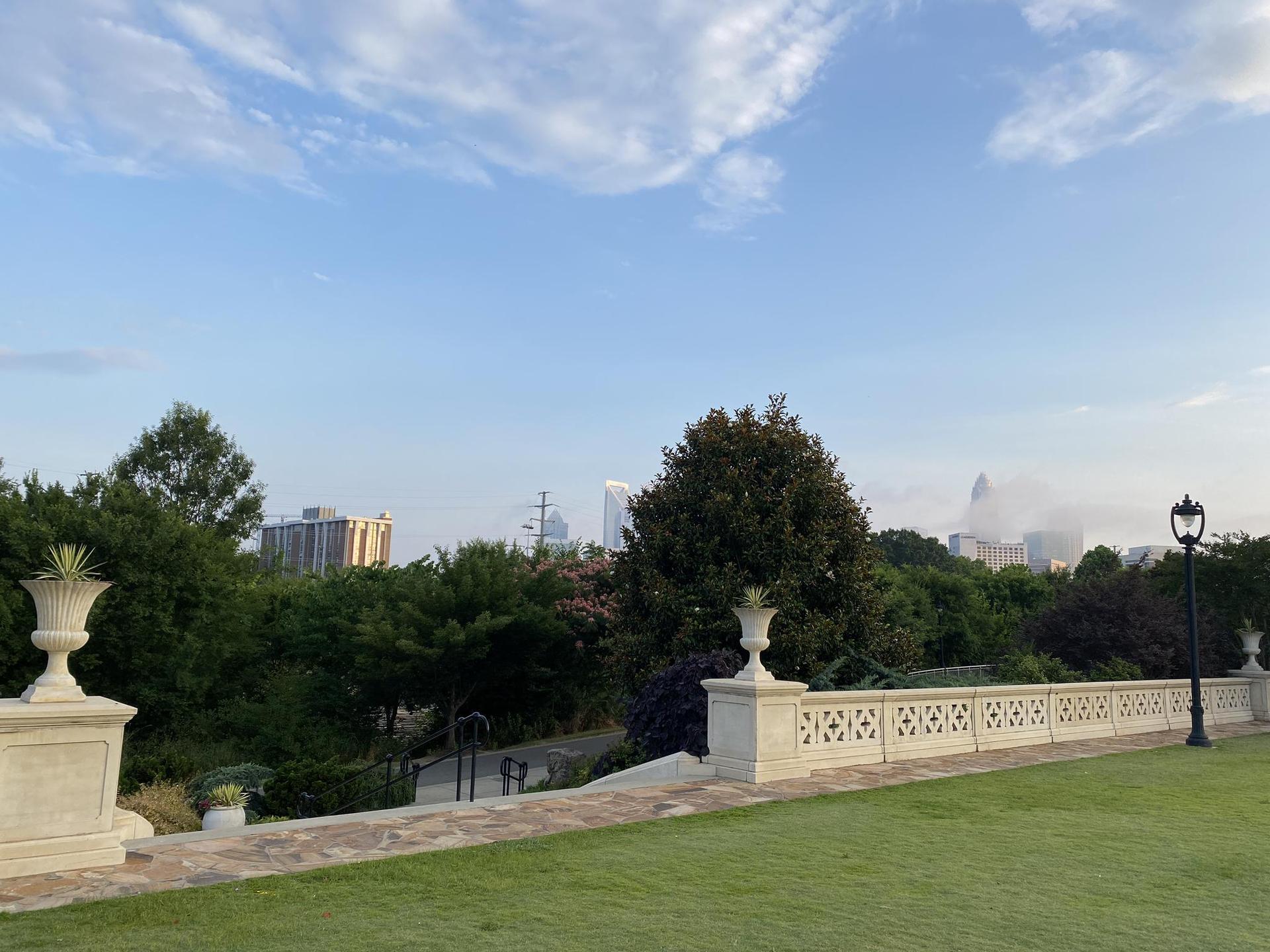 A manicured lawn and stone balustrade overlooking a distant city skyline.