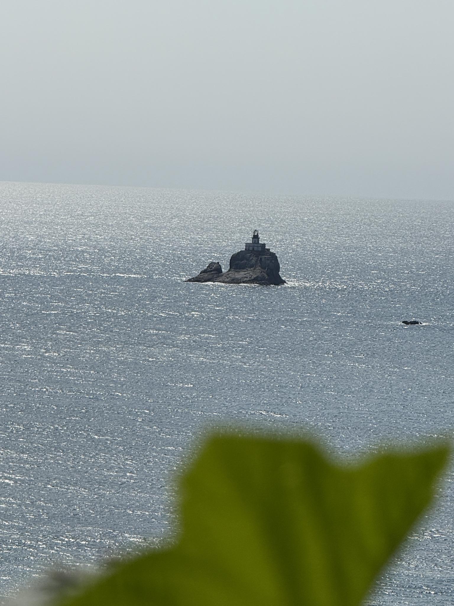 Distant lighthouse on a rocky island in a hazy, sparkling ocean.