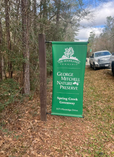 A green banner sign stands by a forest path with parked cars. - Flintridge Loop Trail