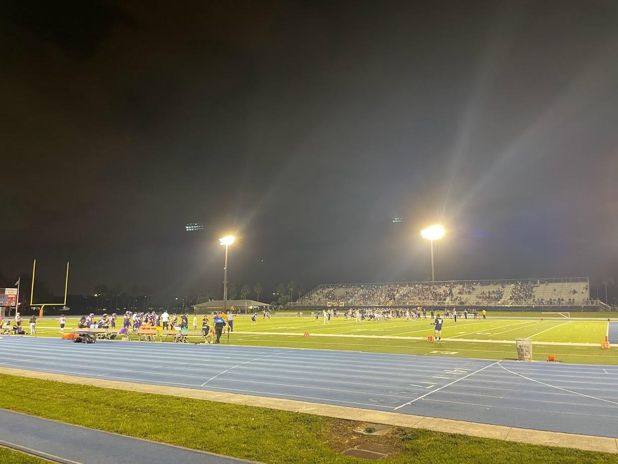 Night game on a lit football field with players and spectators.