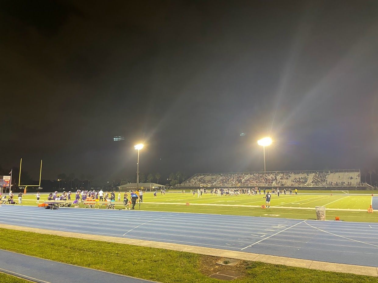 Night game on a lit football field with players and spectators. - Tropical Park loop