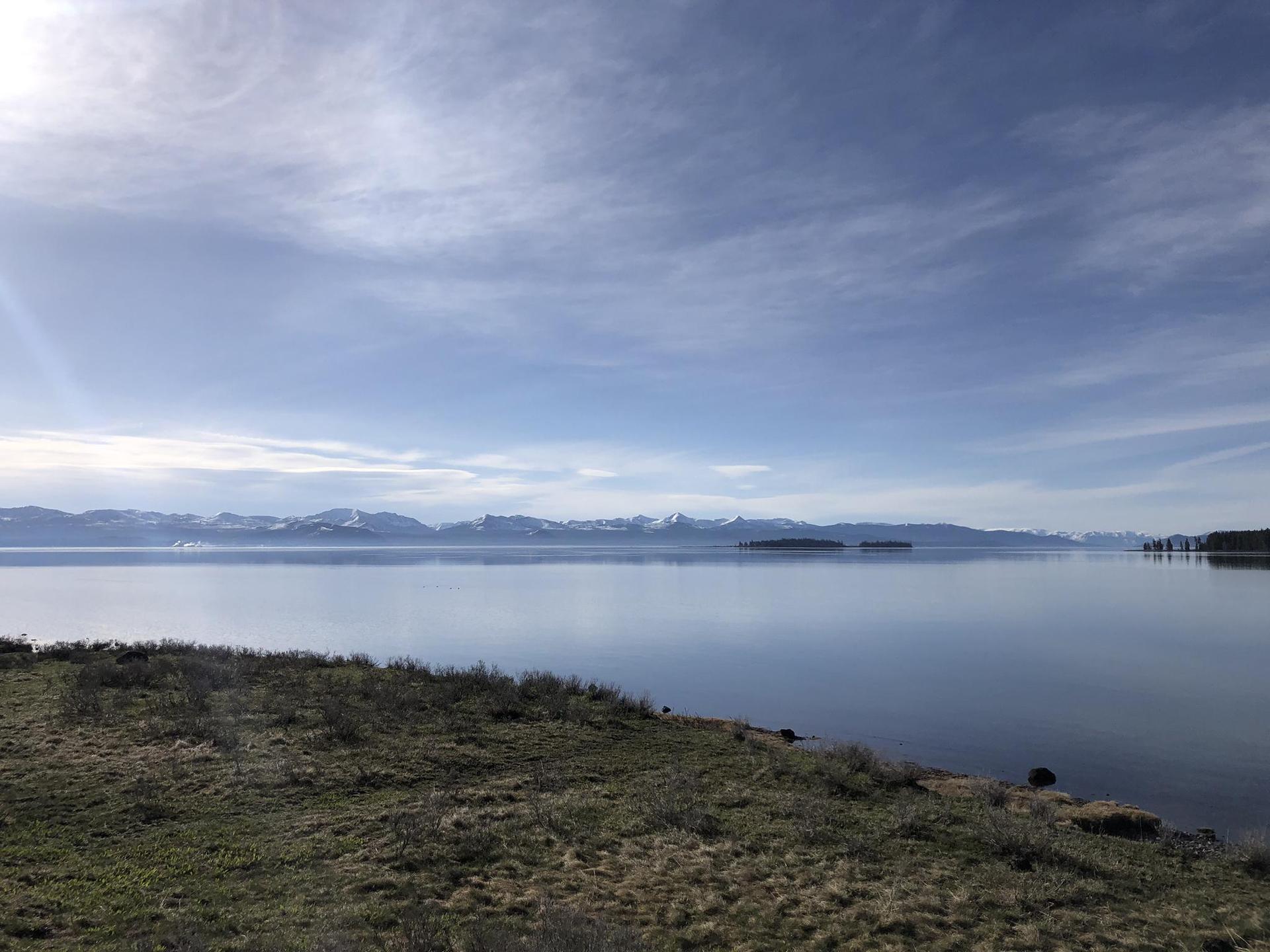 Calm lake with distant snow-capped mountains under a bright, cloudy sky.
