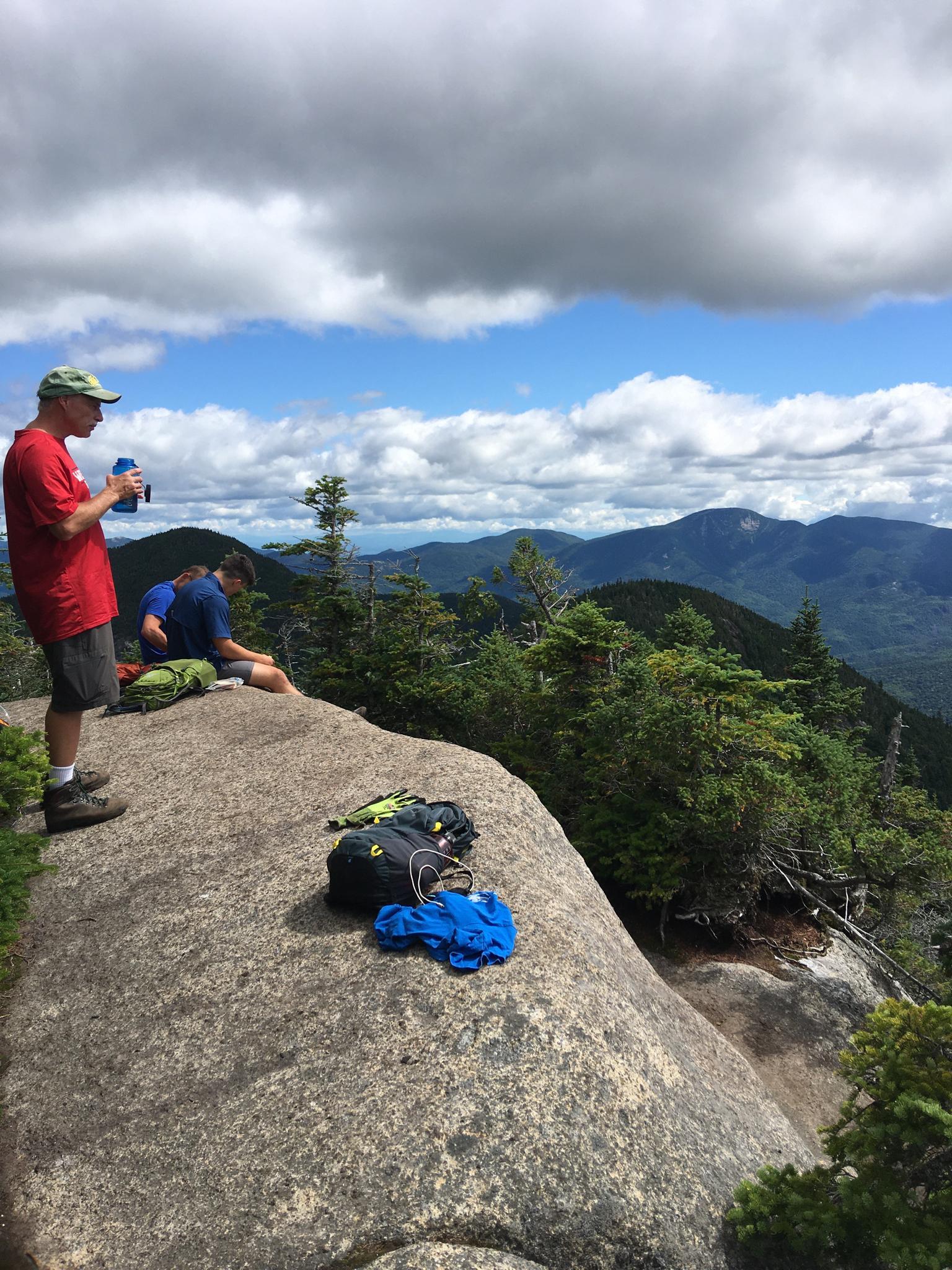 Two hikers rest on a rocky overlook, enjoying a vast mountain vista.