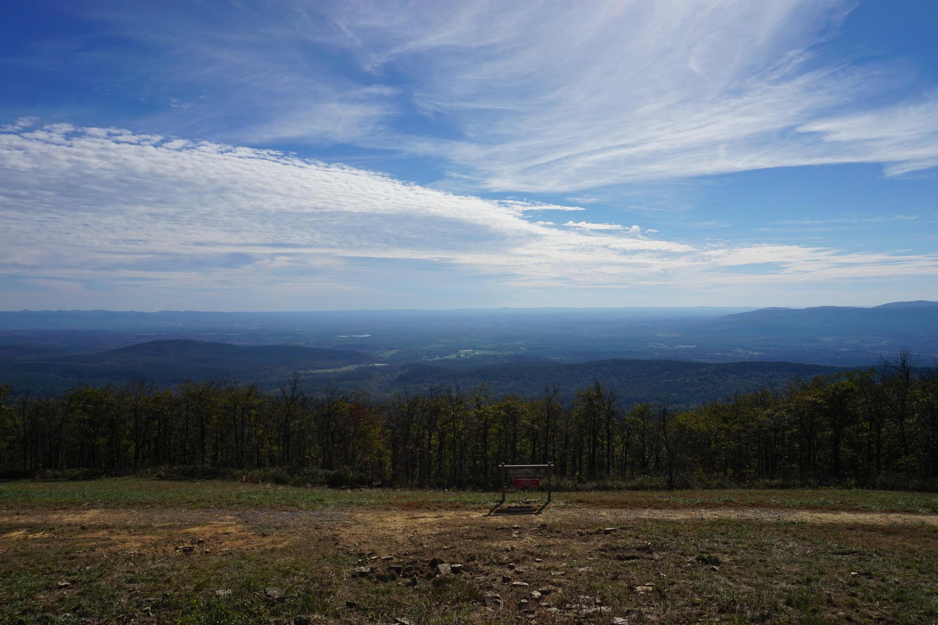 Panoramic view of forested mountains and valleys under a bright, cloudy sky.