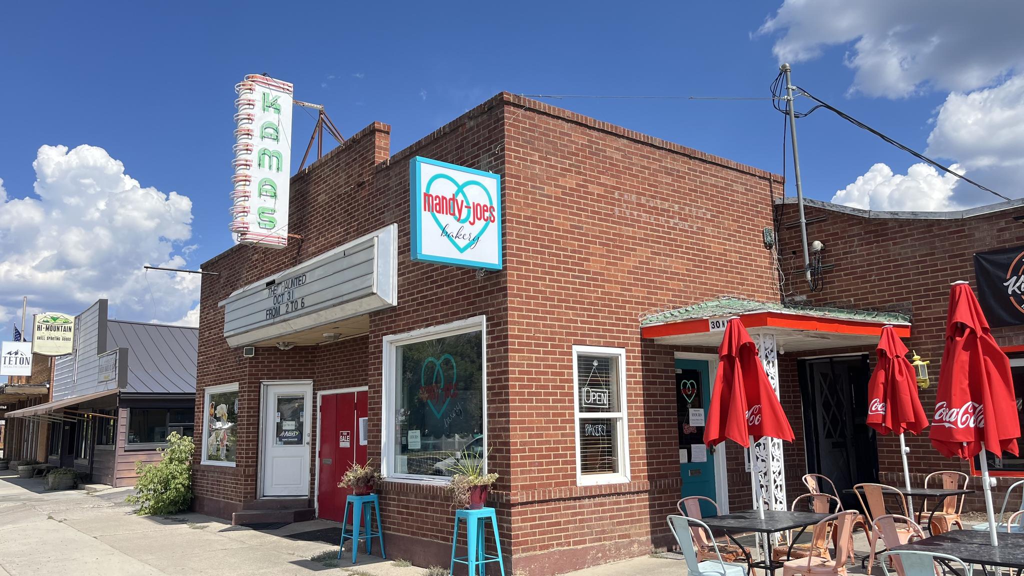 A brick building with red umbrellas and outdoor seating under a bright sky.