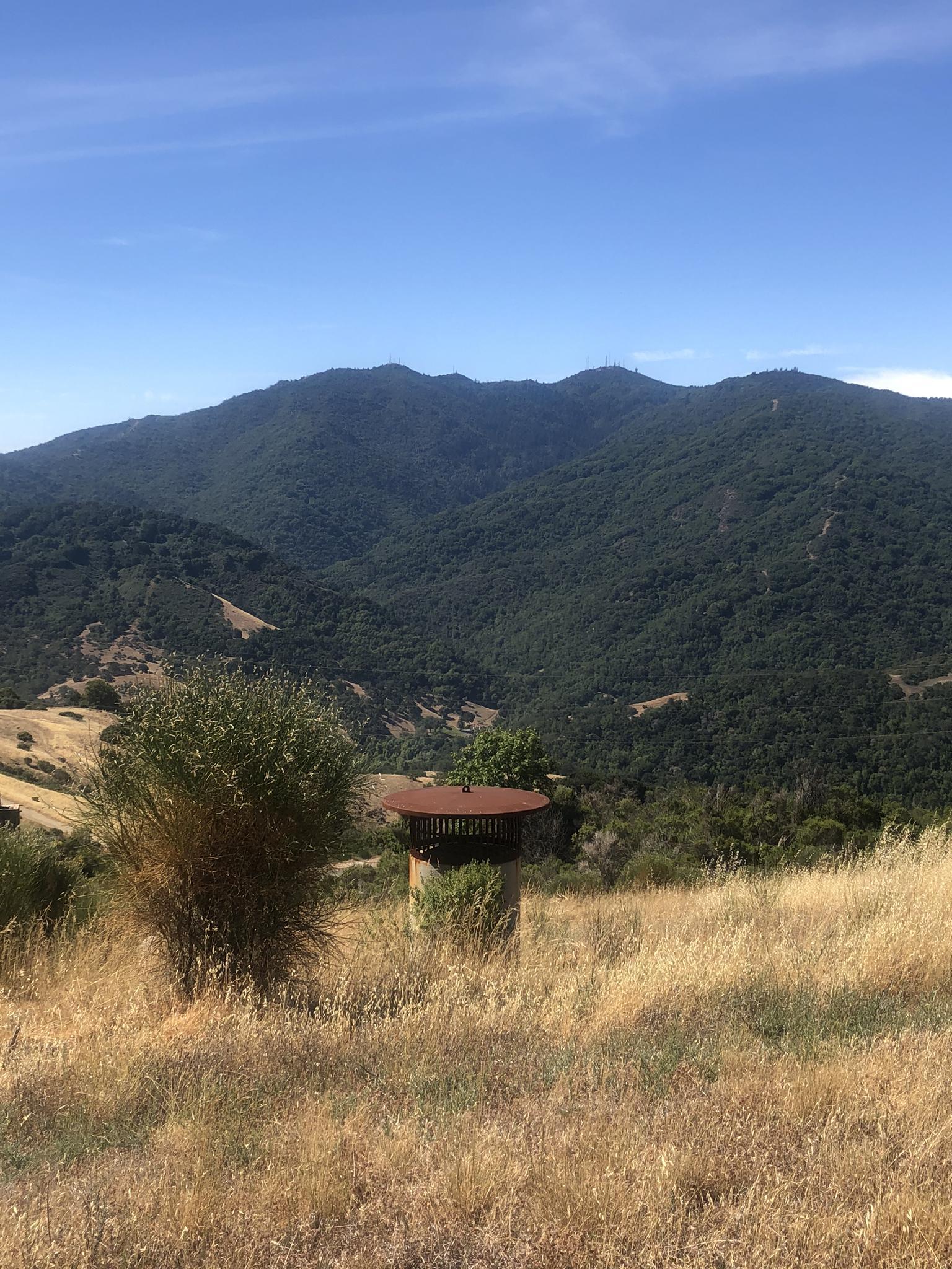 A rustic structure in a dry field, with distant green mountains.