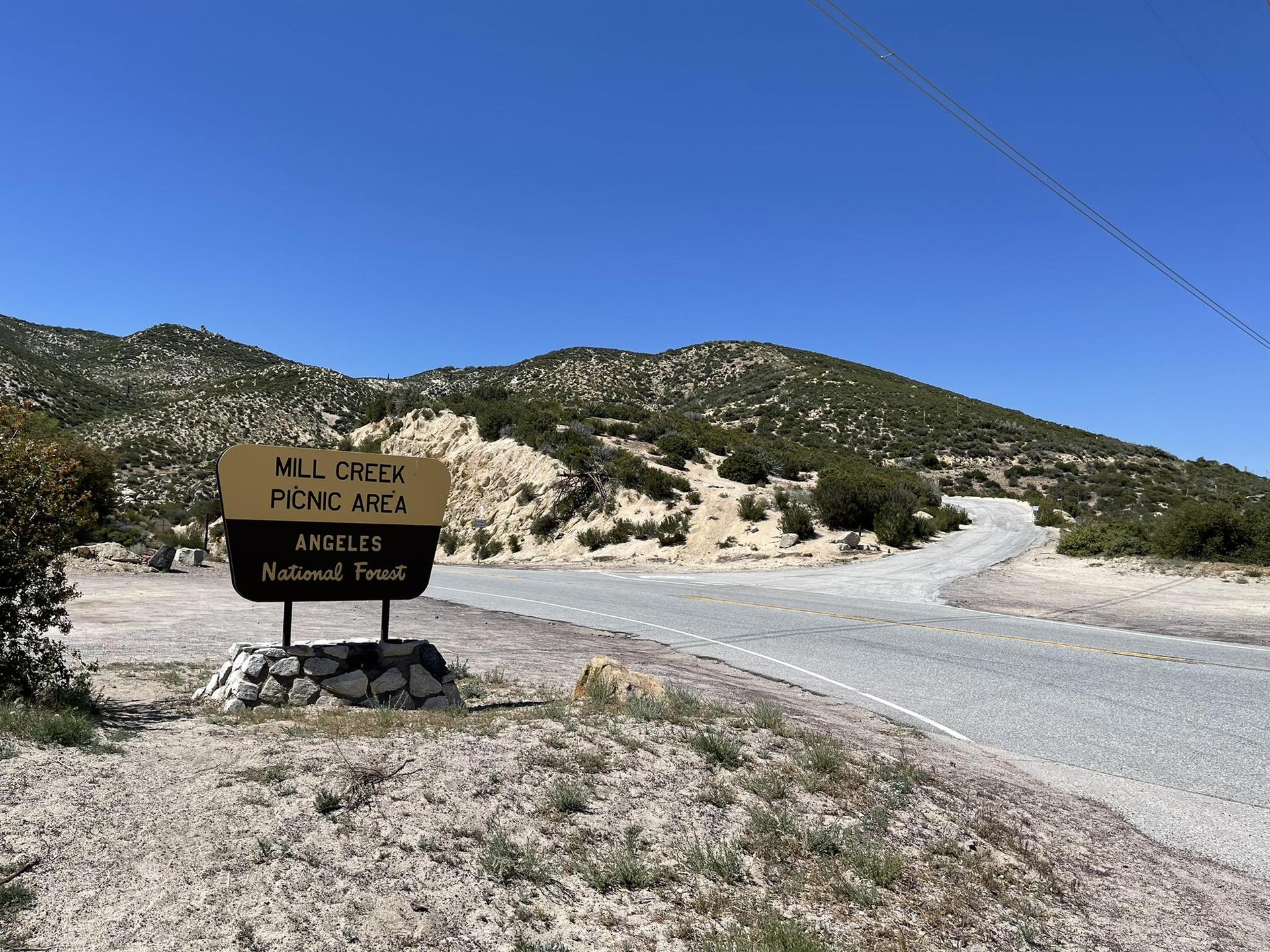 A brown sign on a sunny day next to a paved road and arid mountains.