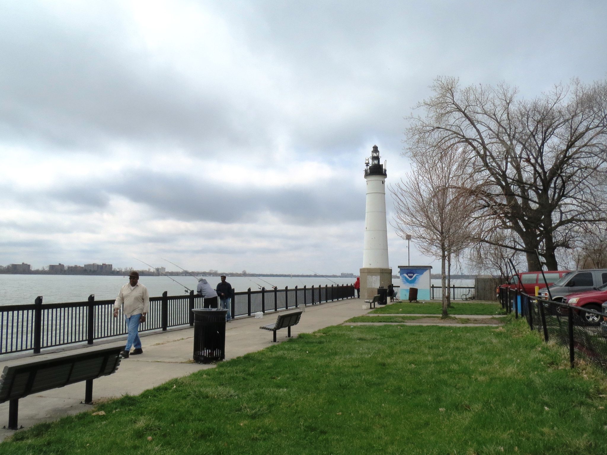 People walk and fish along a waterfront promenade with a white lighthouse under a cloudy sky. - Fox Creek loop from Trombly Elementary School