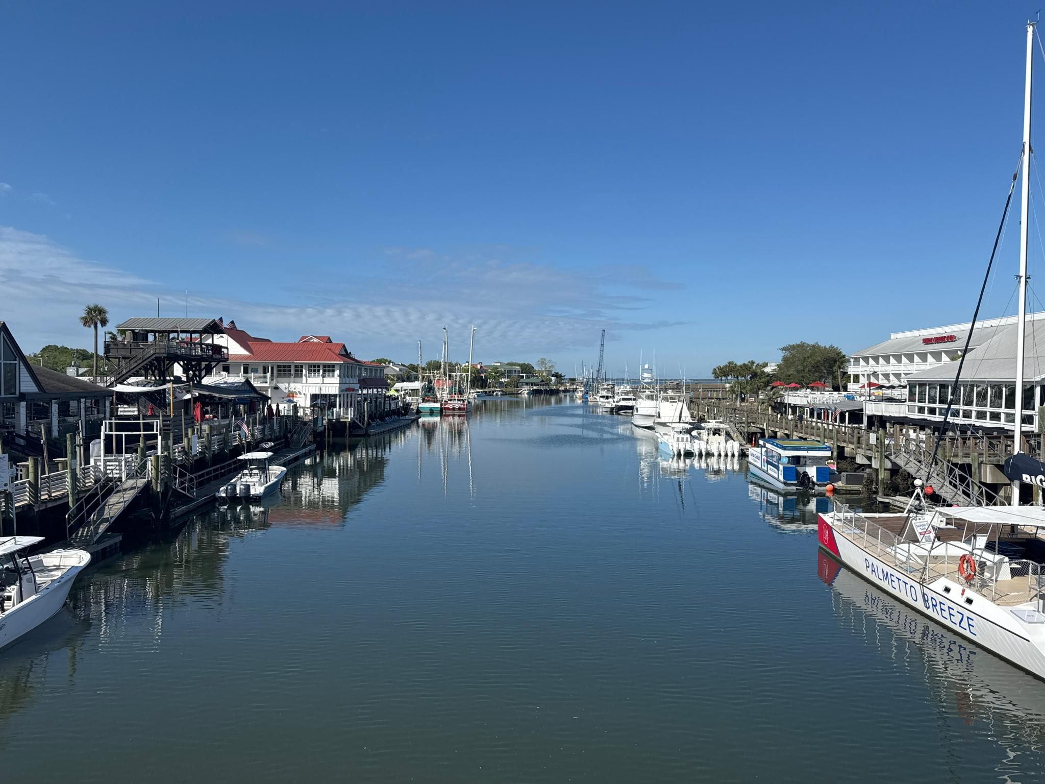 Boats docked along a narrow waterway lined with buildings on a sunny day. - East Coast Greenway: Mount Pleasant