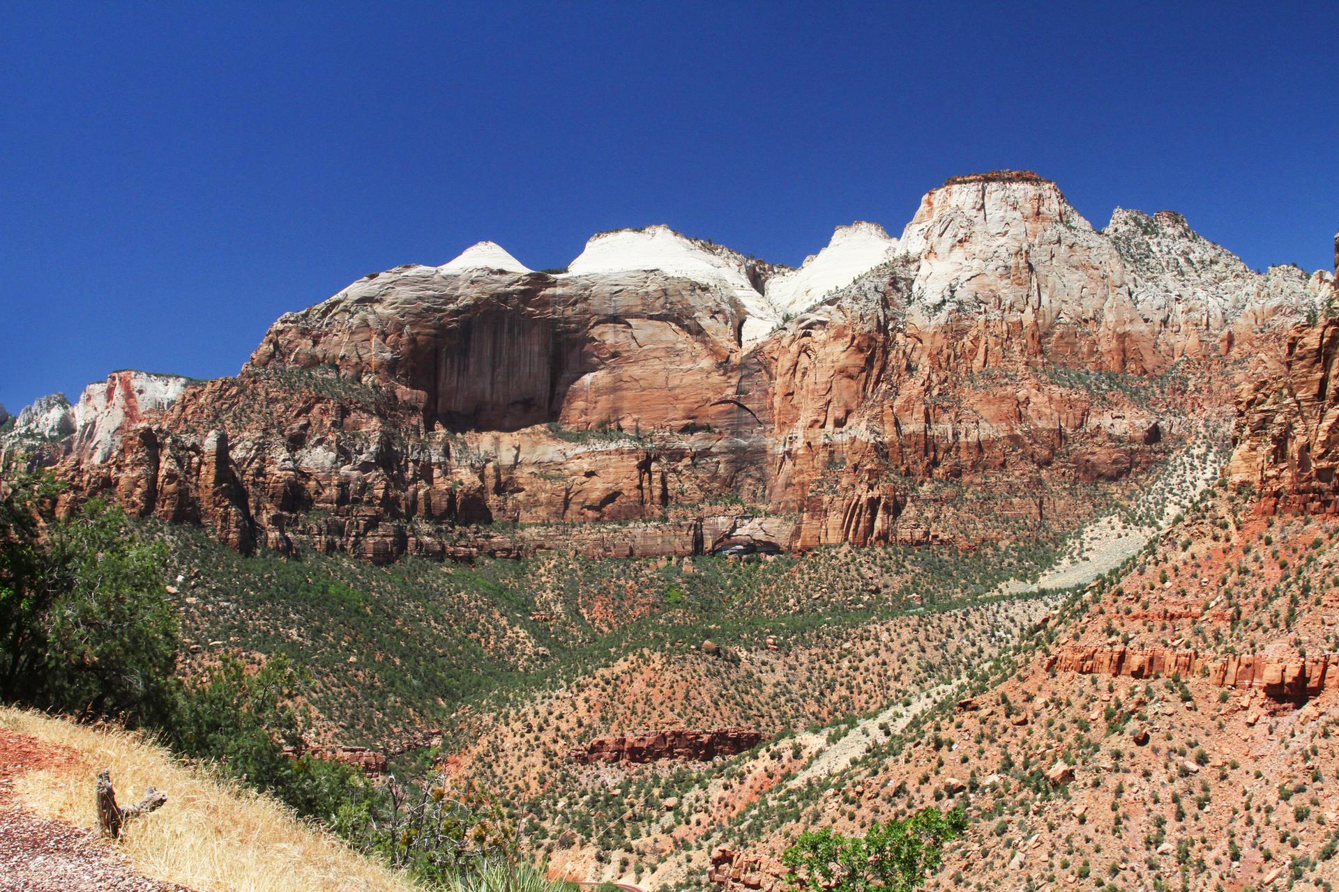 Majestic red and white rock formations with green vegetation under bright blue sky.
