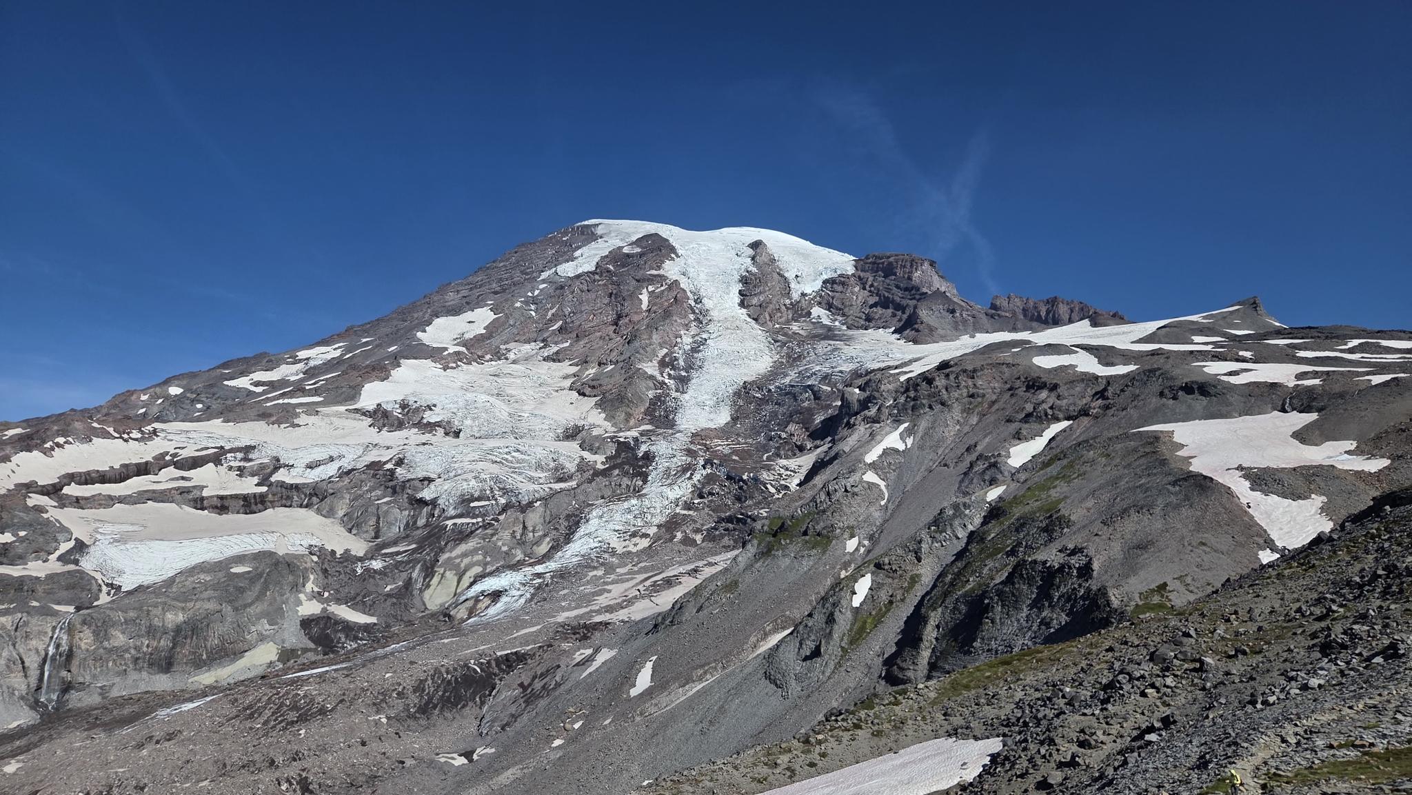 Large snow-capped mountain with glaciers and rocky slopes under a clear blue sky.