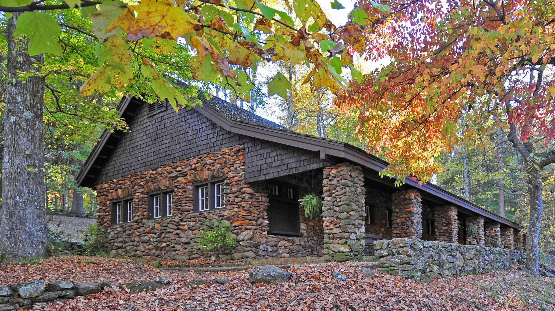Rustic stone and wood building with a porch, surrounded by colorful autumn foliage.
