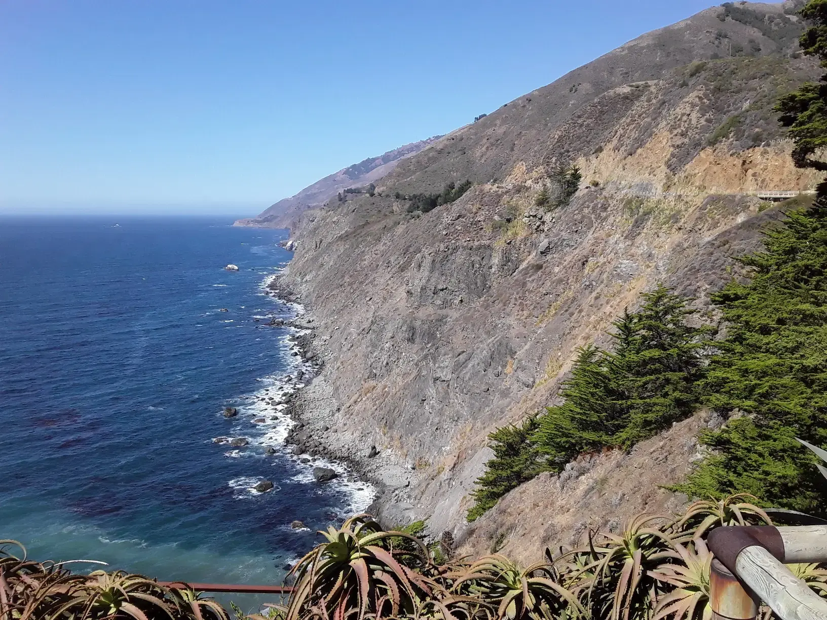 Steep rocky cliff overlooking a deep blue ocean on a sunny day.