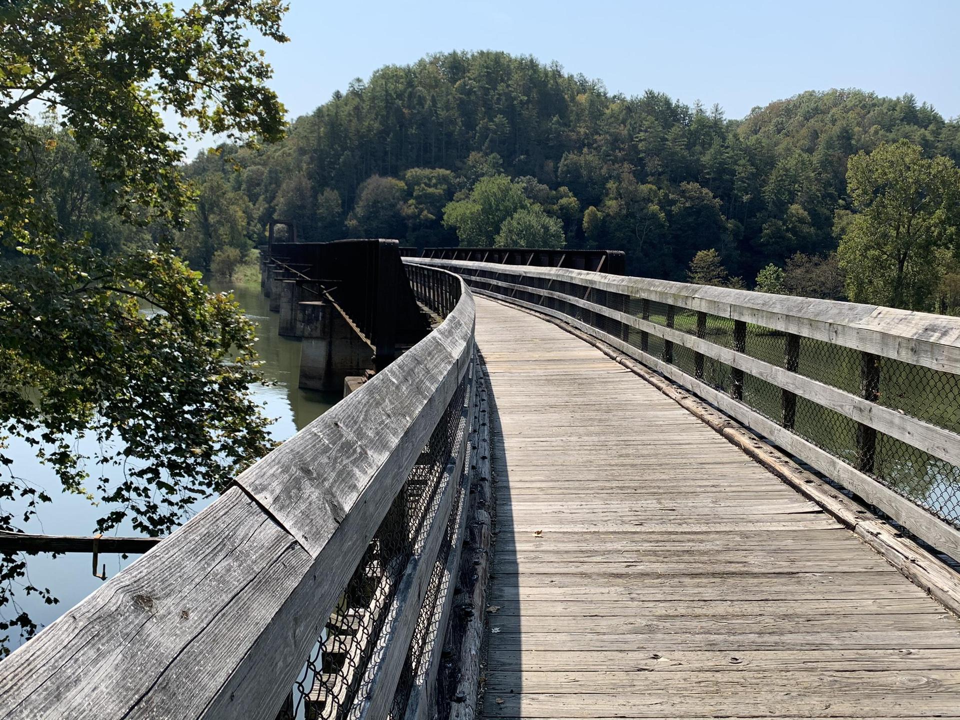 Long wooden bridge curving over water with distant forested hills.