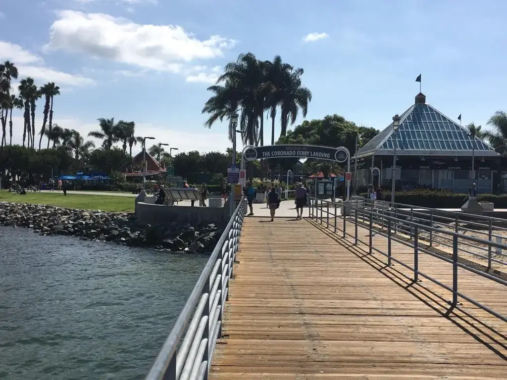 People walk on a wooden pier leading to a building and palm trees.