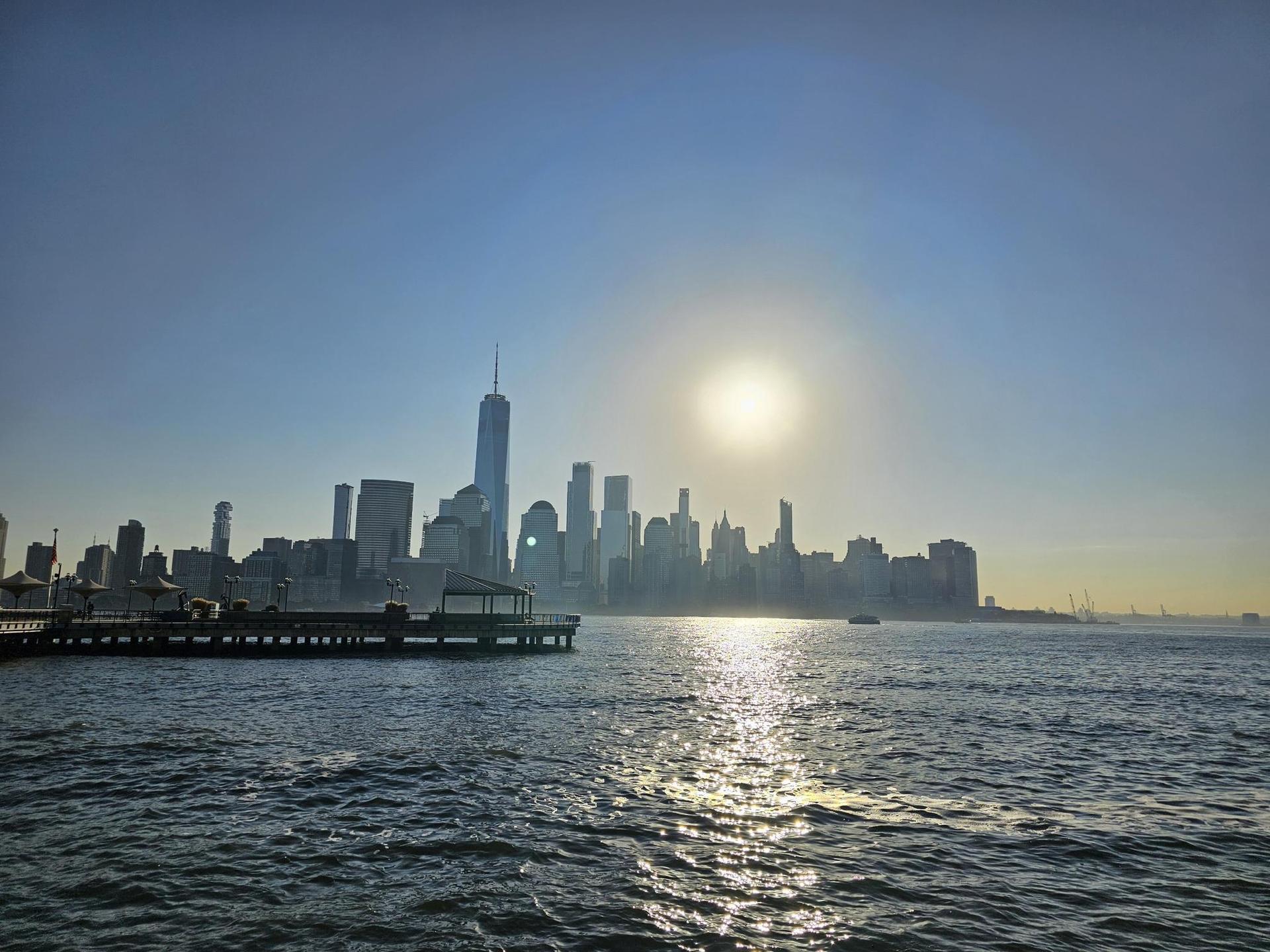 Sun setting over a city skyline across water, with a pier in the foreground.