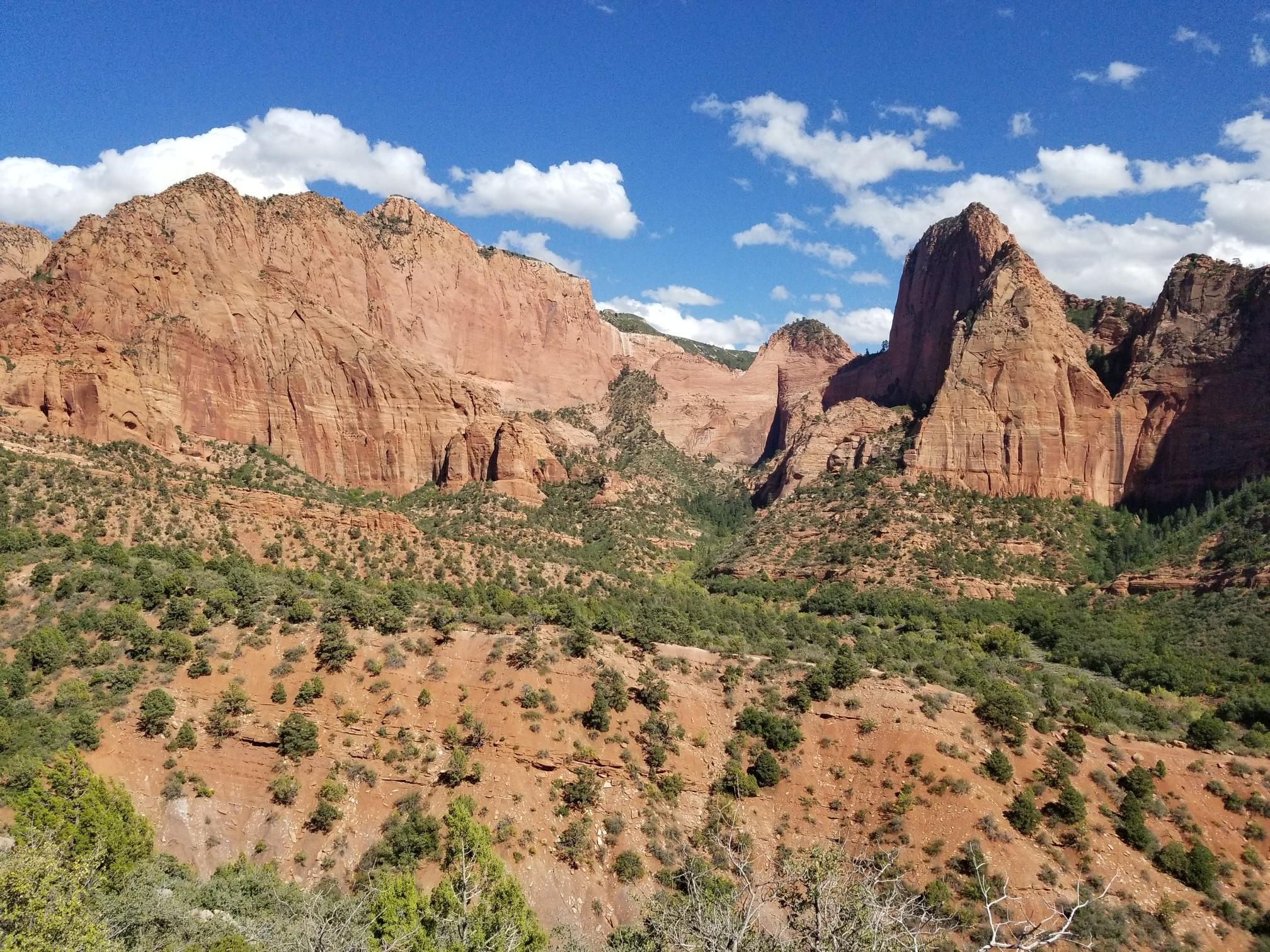 Expansive view of red rock formations and scrub-covered hills under a partly cloudy sky.
