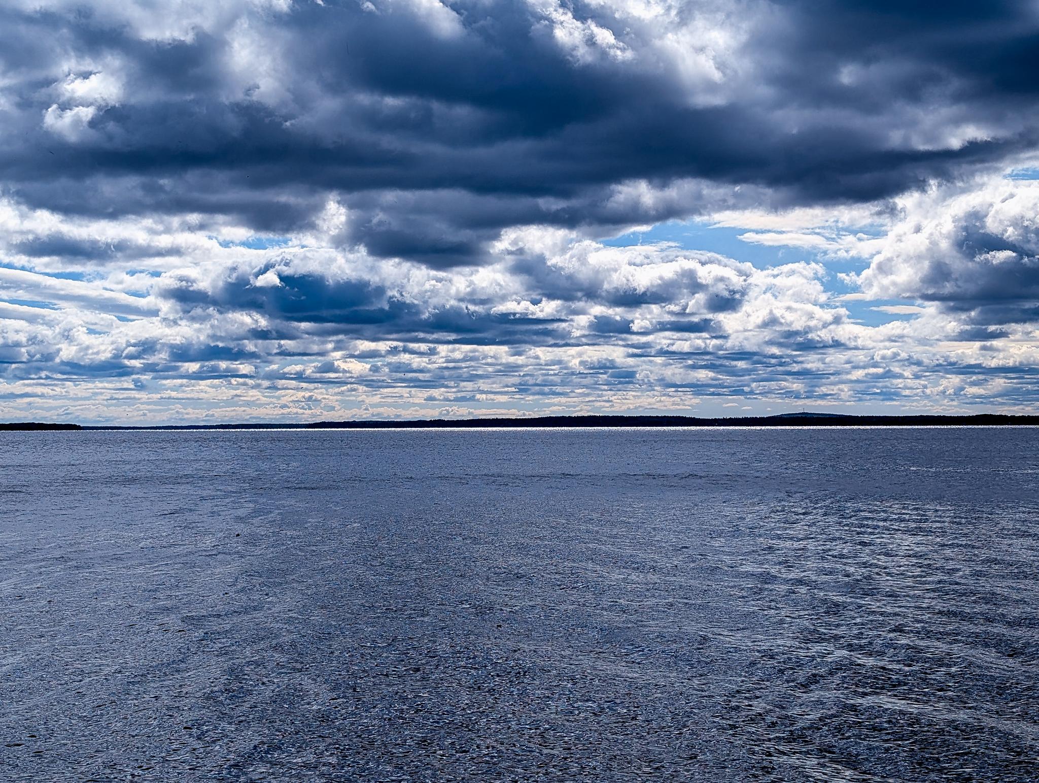 Vast body of water under a dramatic, cloudy sky with distant land.