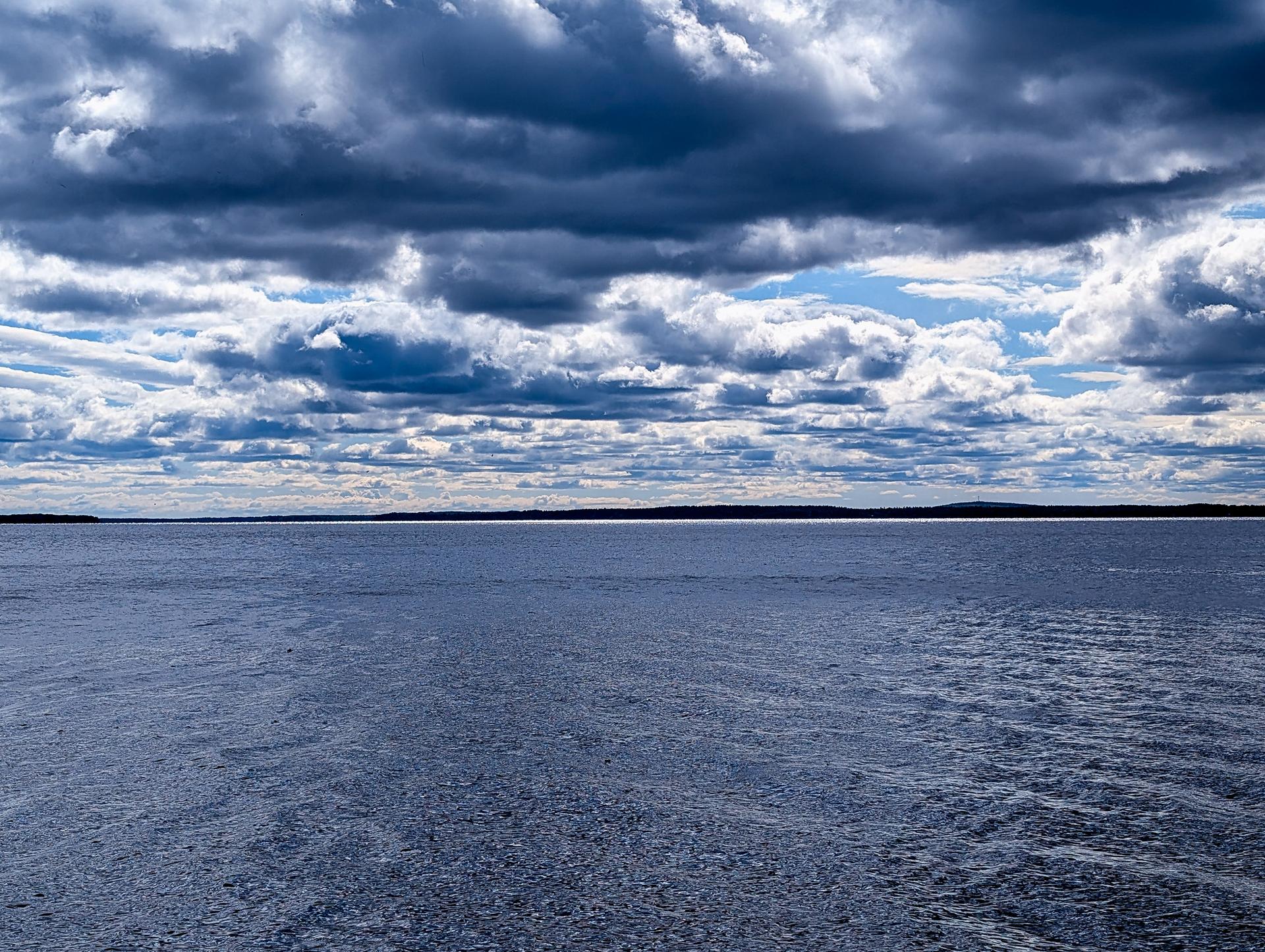 Vast body of water under a dramatic, cloudy sky with distant land.