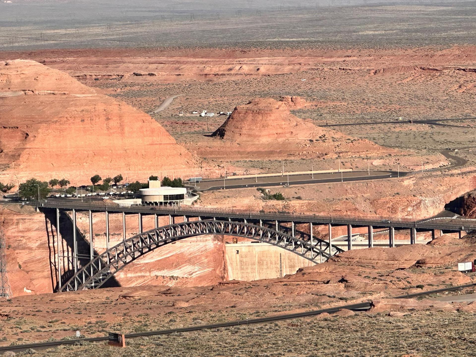 Overhead view of a large steel arch bridge spanning a desert canyon.